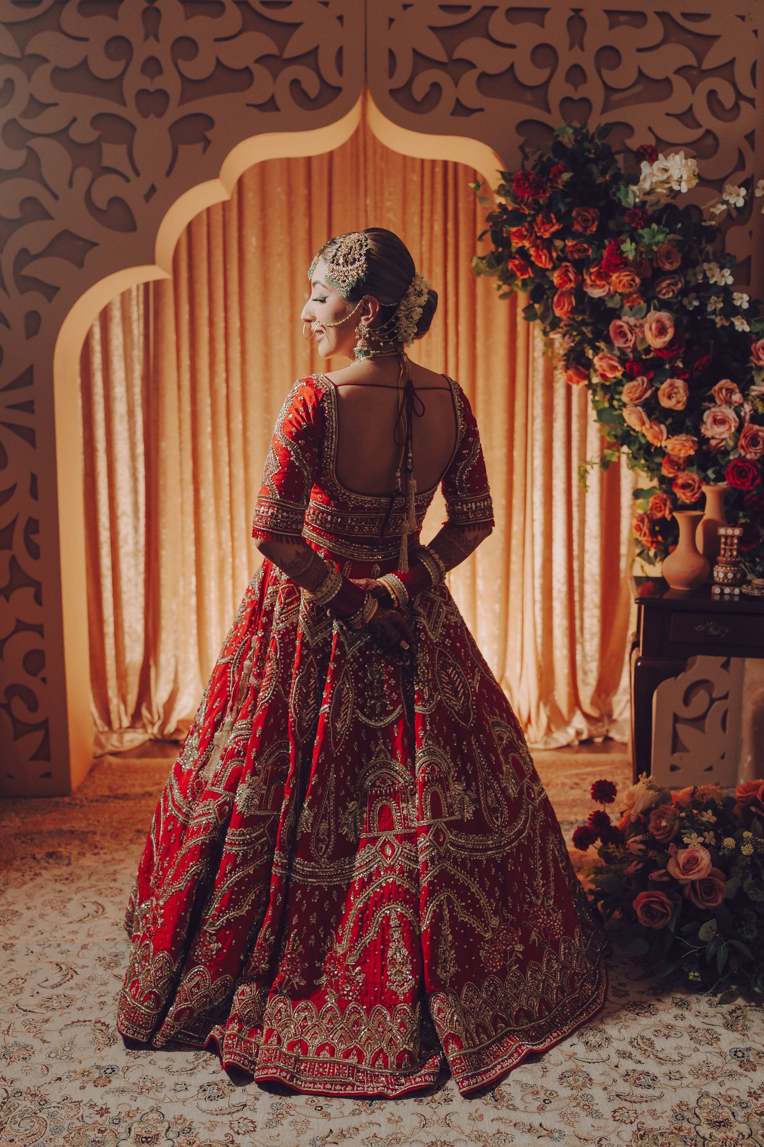 Stunning red and gold heavily embroidered bridal lehenga displayed in an elegant setting with floral decorations.