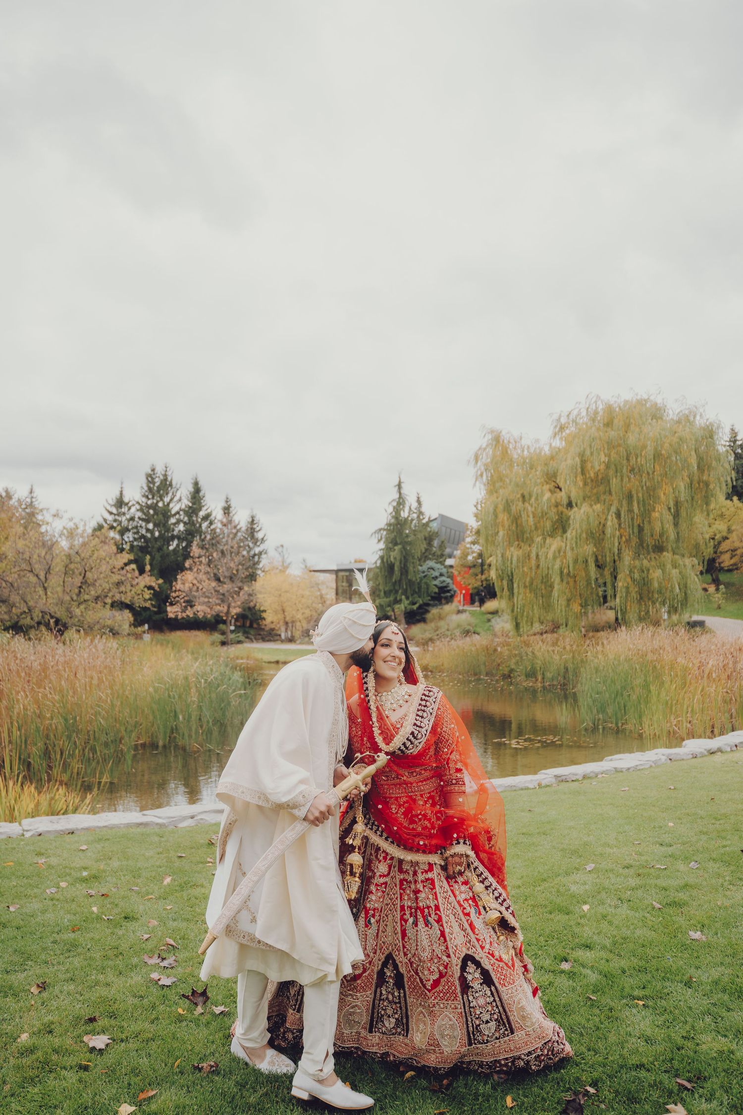 Couple in traditional Indian wedding attire embracing in scenic park setting.