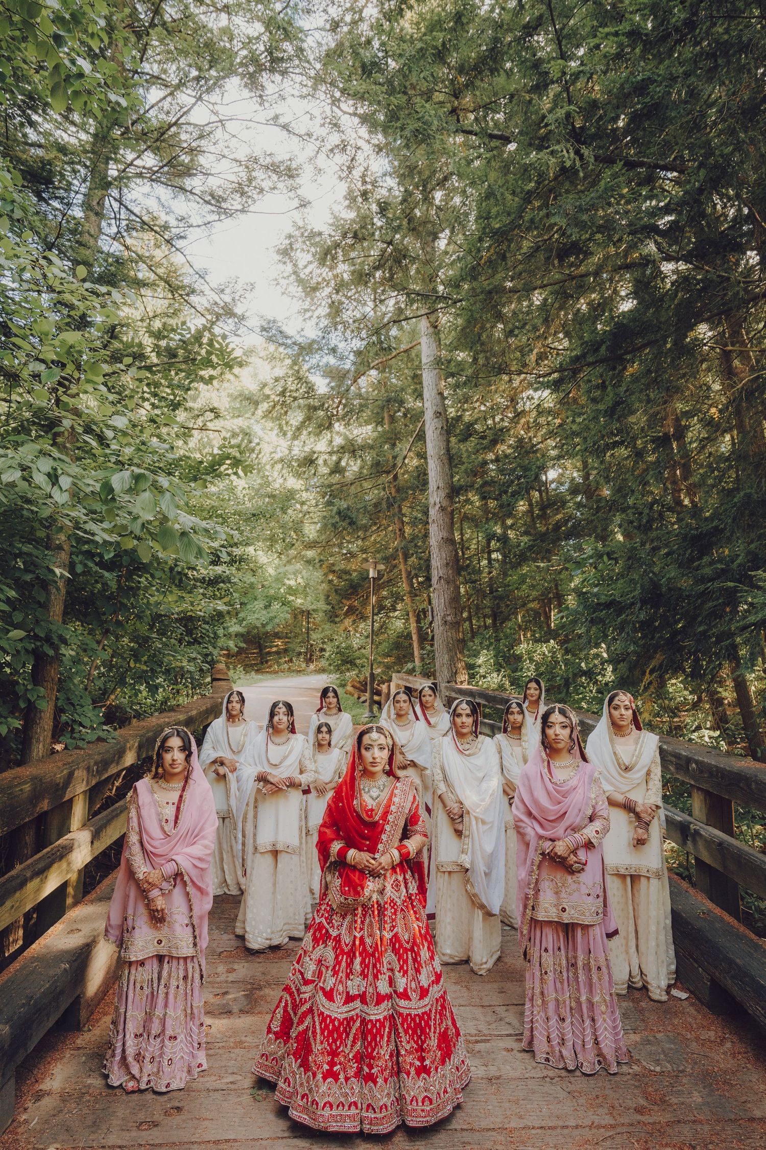 Wedding party in traditional Indian attire walking along wooden bridge path through trees.