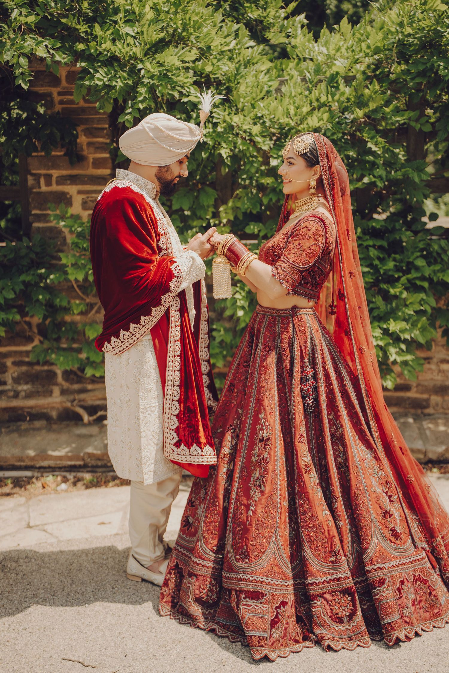 Traditional Indian wedding couple shares intimate moments in their ornate red and gold wedding attire outdoors.