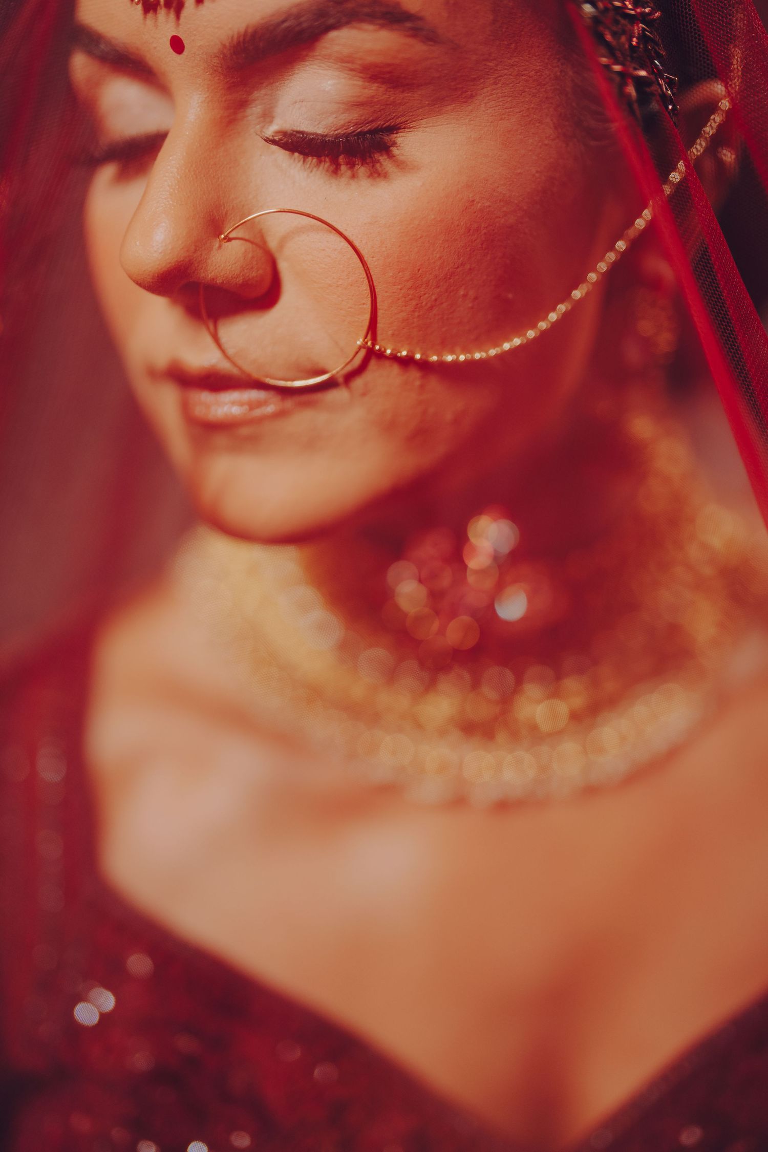 Close-up details of traditional Indian bridal jewelry and makeup in rich red tones.