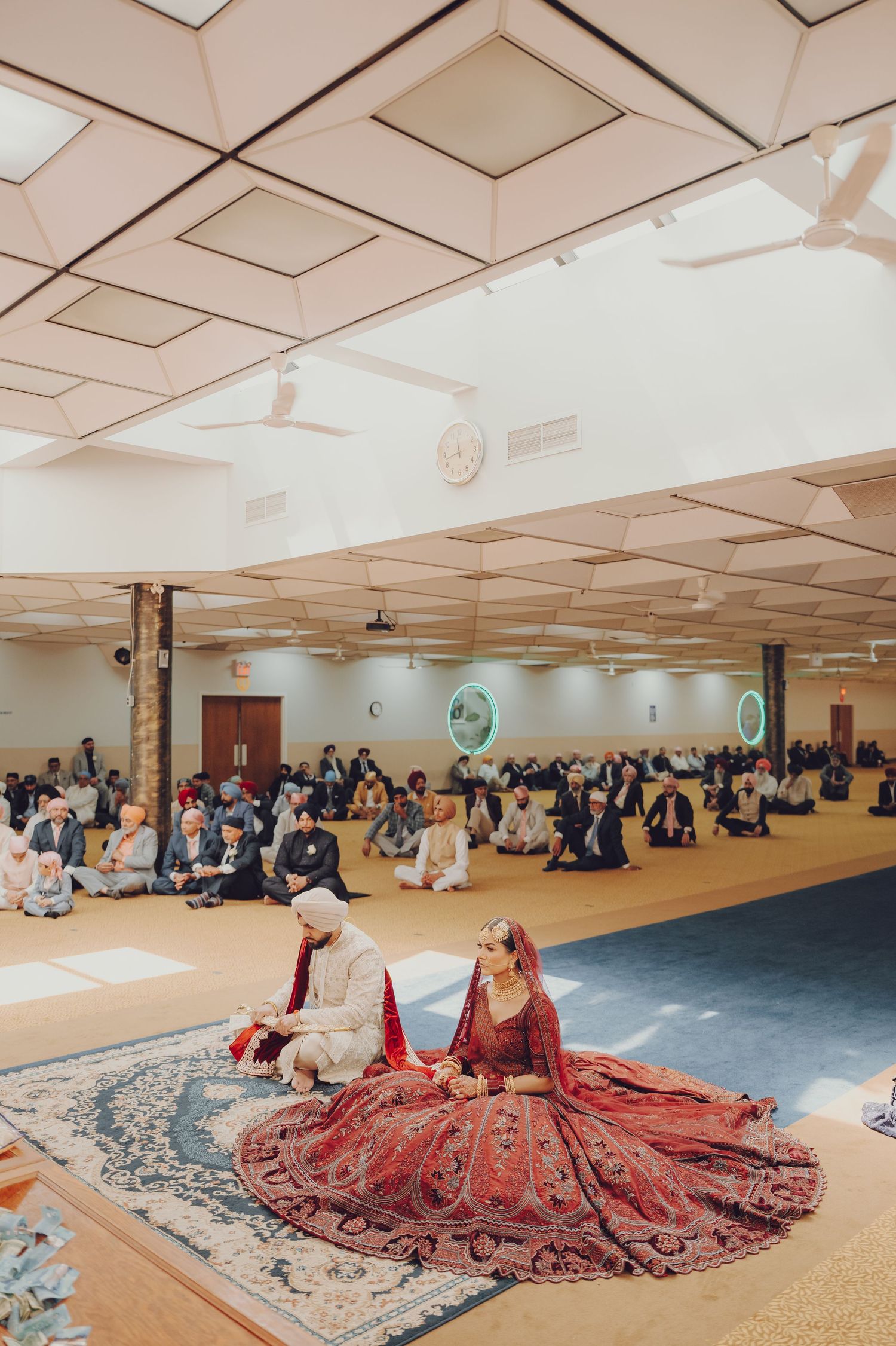 Wide view of traditional Sikh wedding ceremony in a large hall with guests seated on floor.