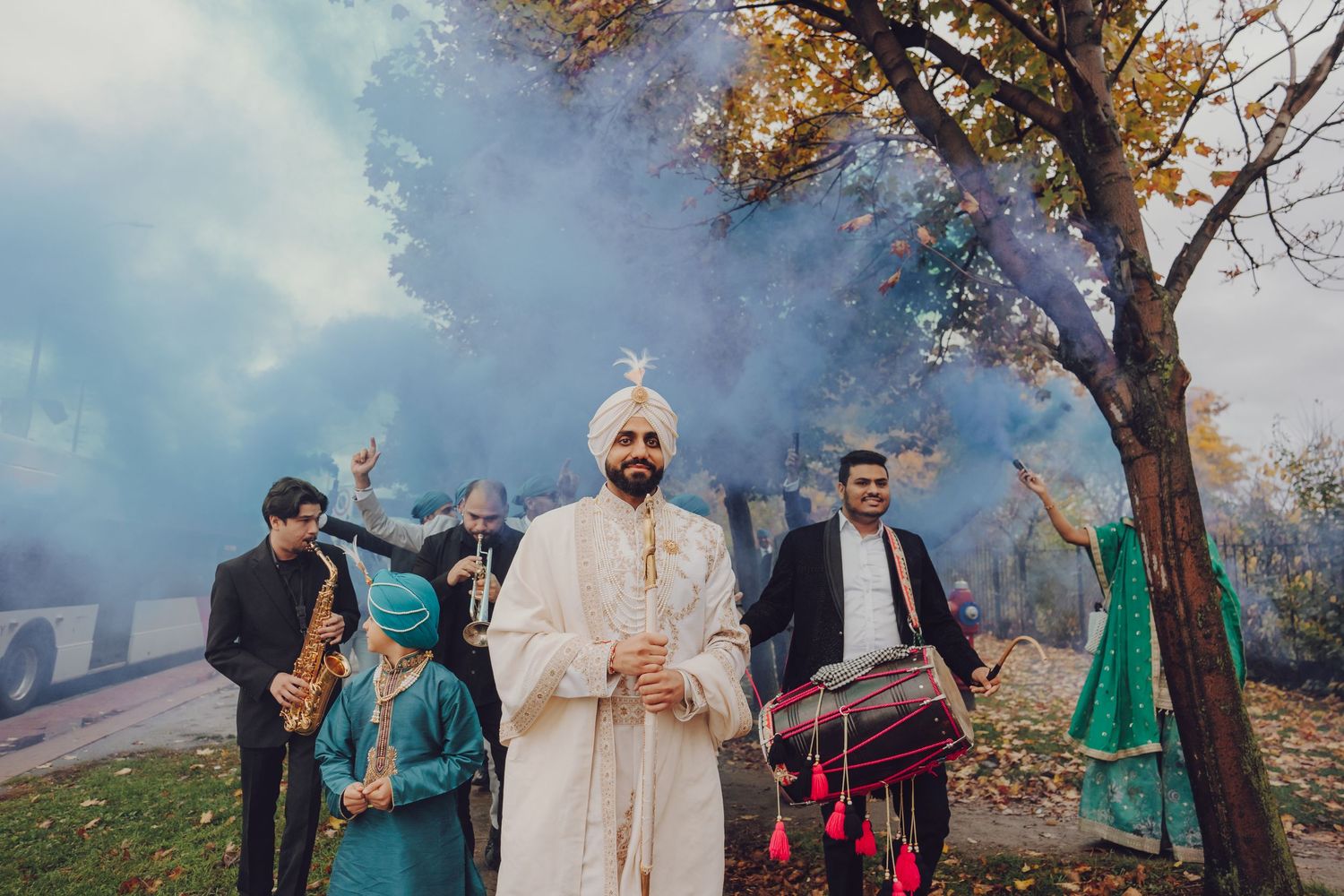 Group gathering outdoors under autumn trees wearing traditional Indian attire at a cultural celebration.