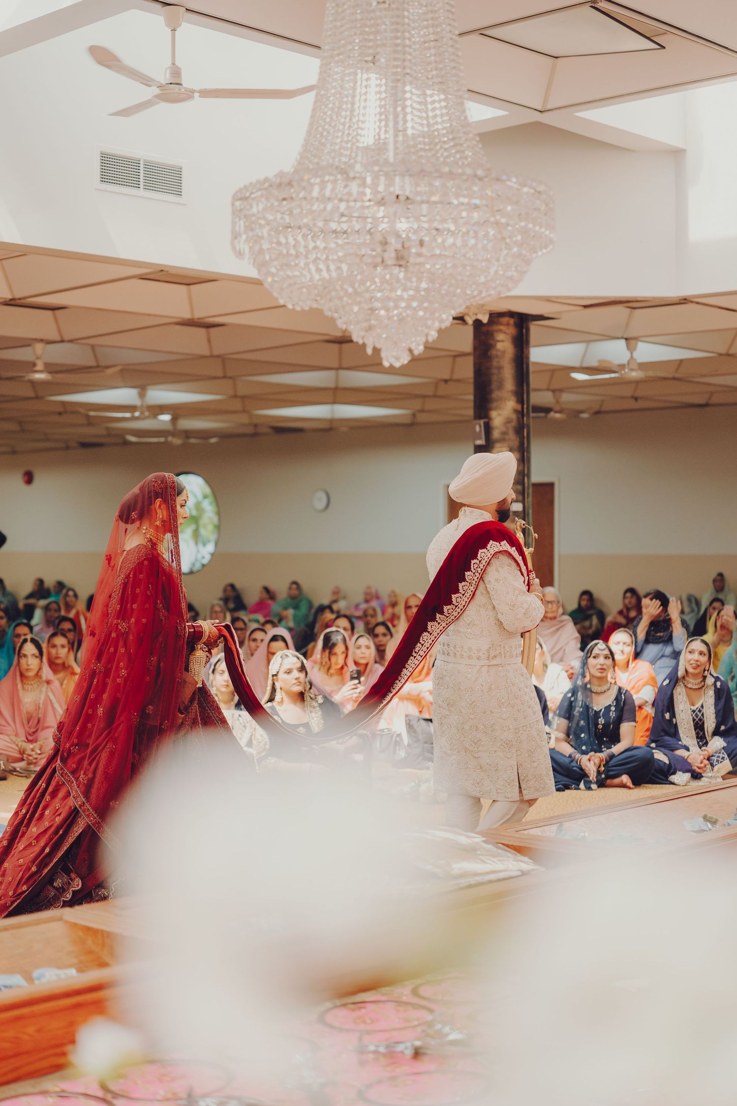 Wedding ceremony venue with crystal chandeliers and guests seated in a large hall.
