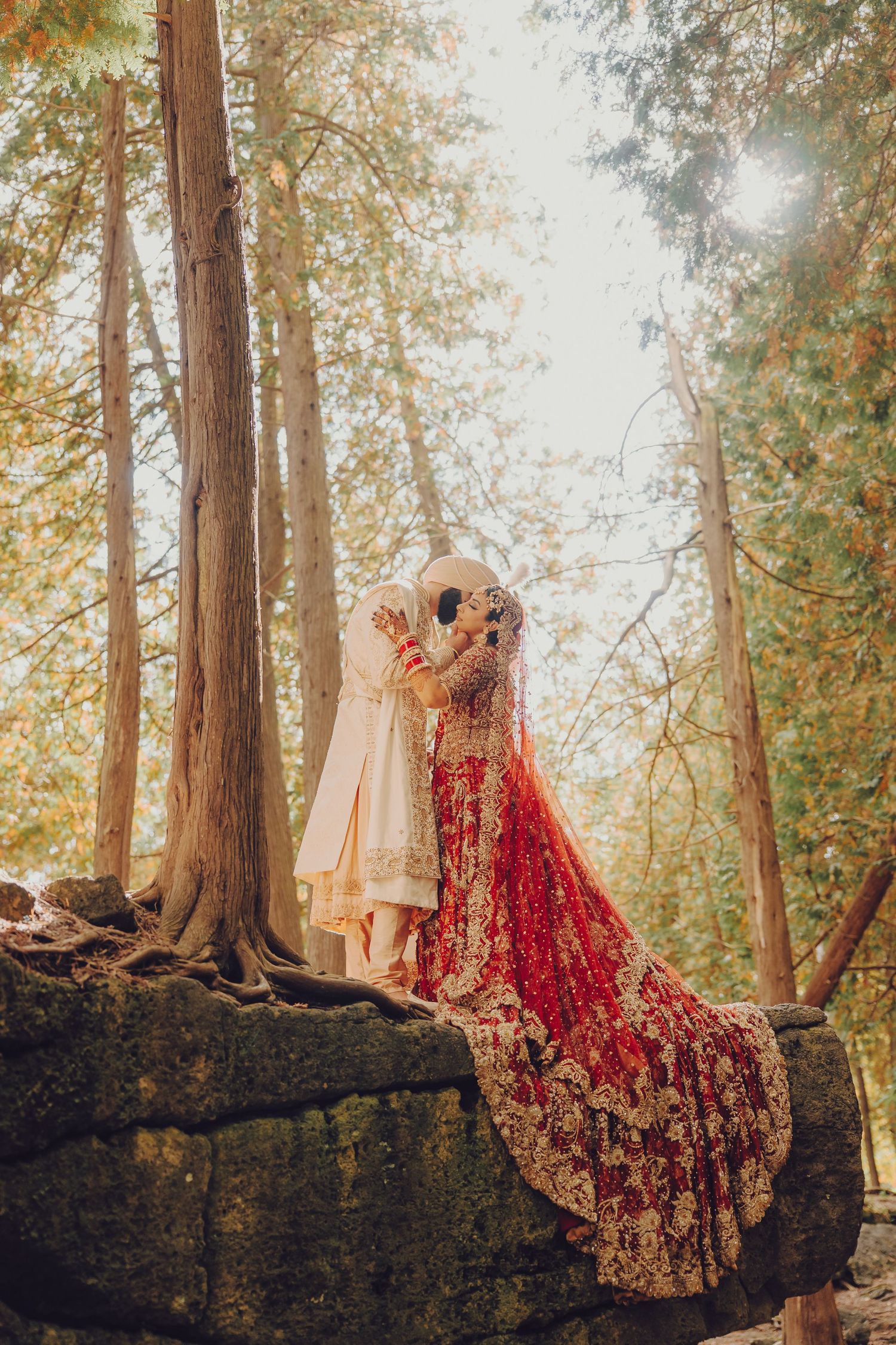 Traditional Indian wedding attire including red lehenga and beige sherwani displayed on rocks in a misty forest setting.