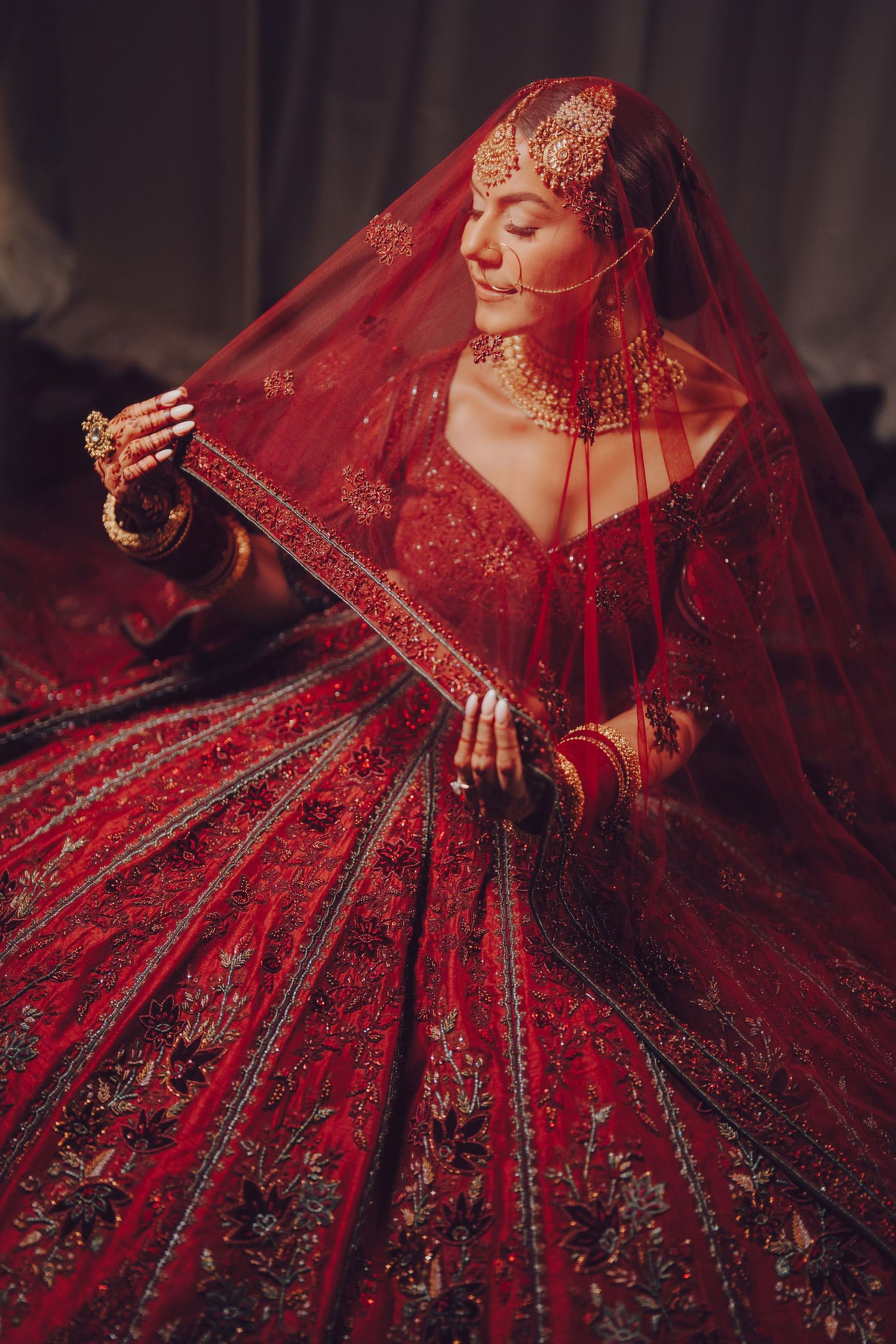 Luxurious red bridal lehenga with intricate gold embroidery and detailed embellishments in dramatic lighting.