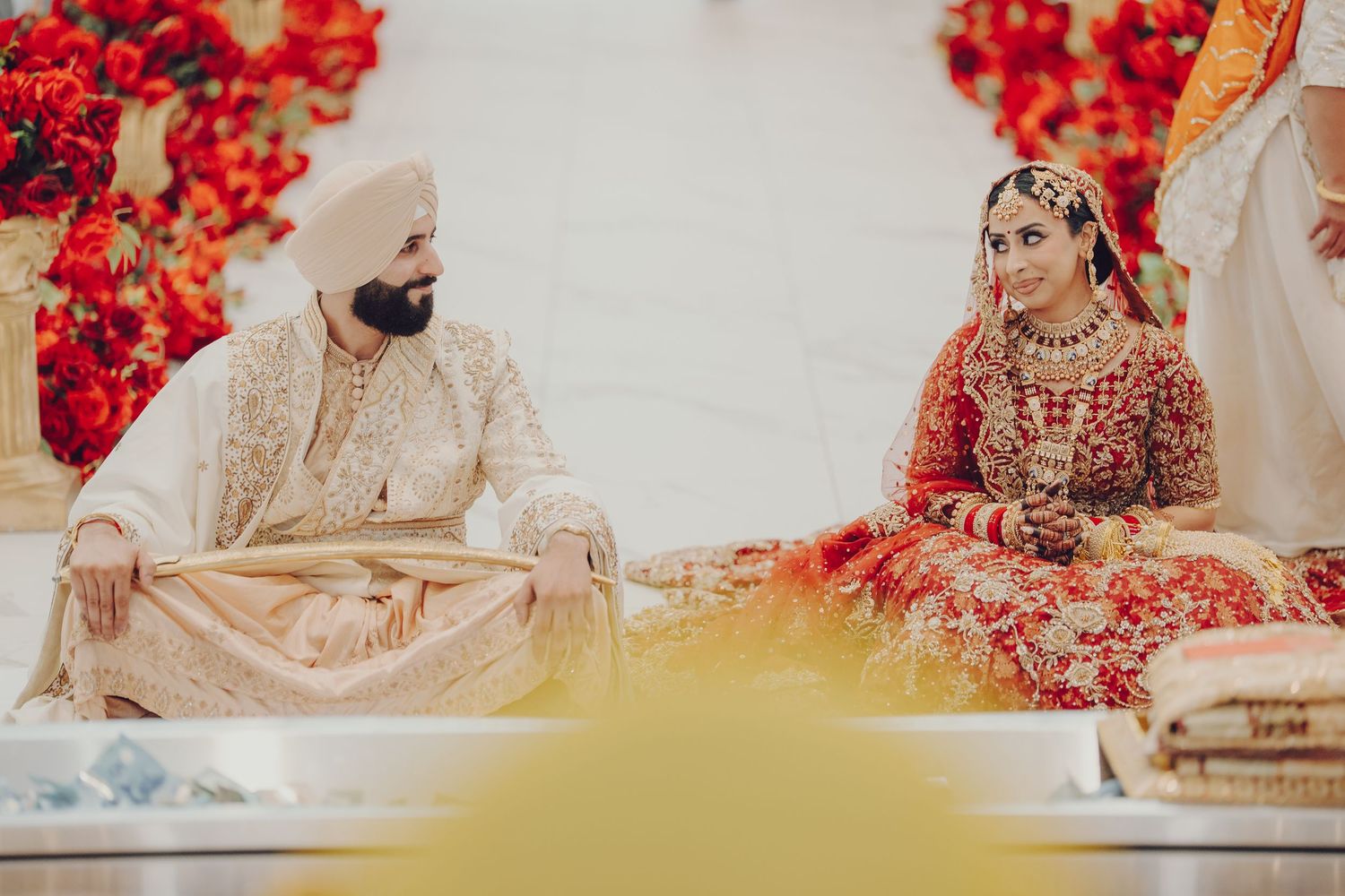 Traditional Indian wedding ceremony with red floral decor and ornate attire in warm tones.