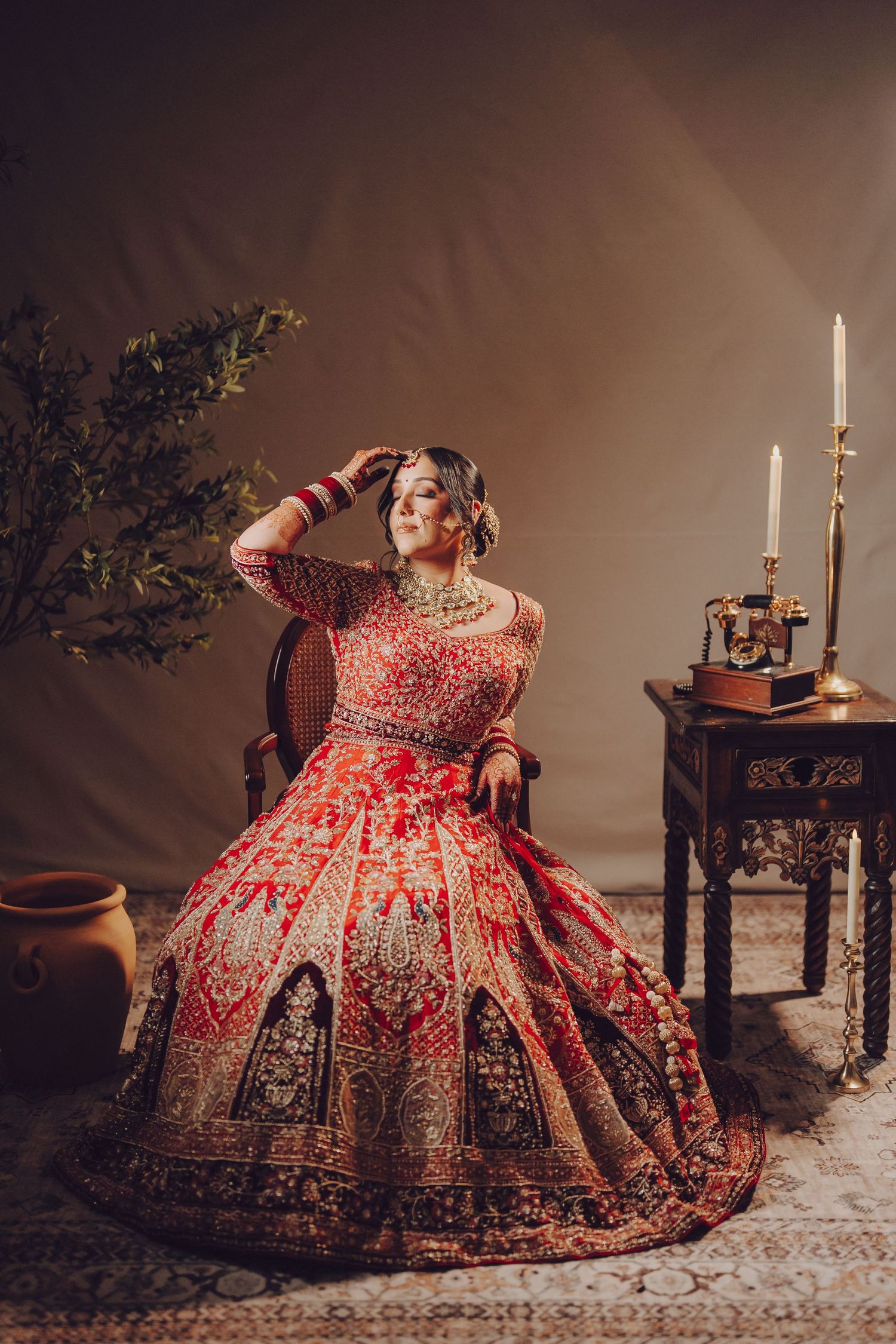 Ornate red and gold traditional Indian bridal lehenga displayed in elegant indoor photoshoot with candlelight setting.