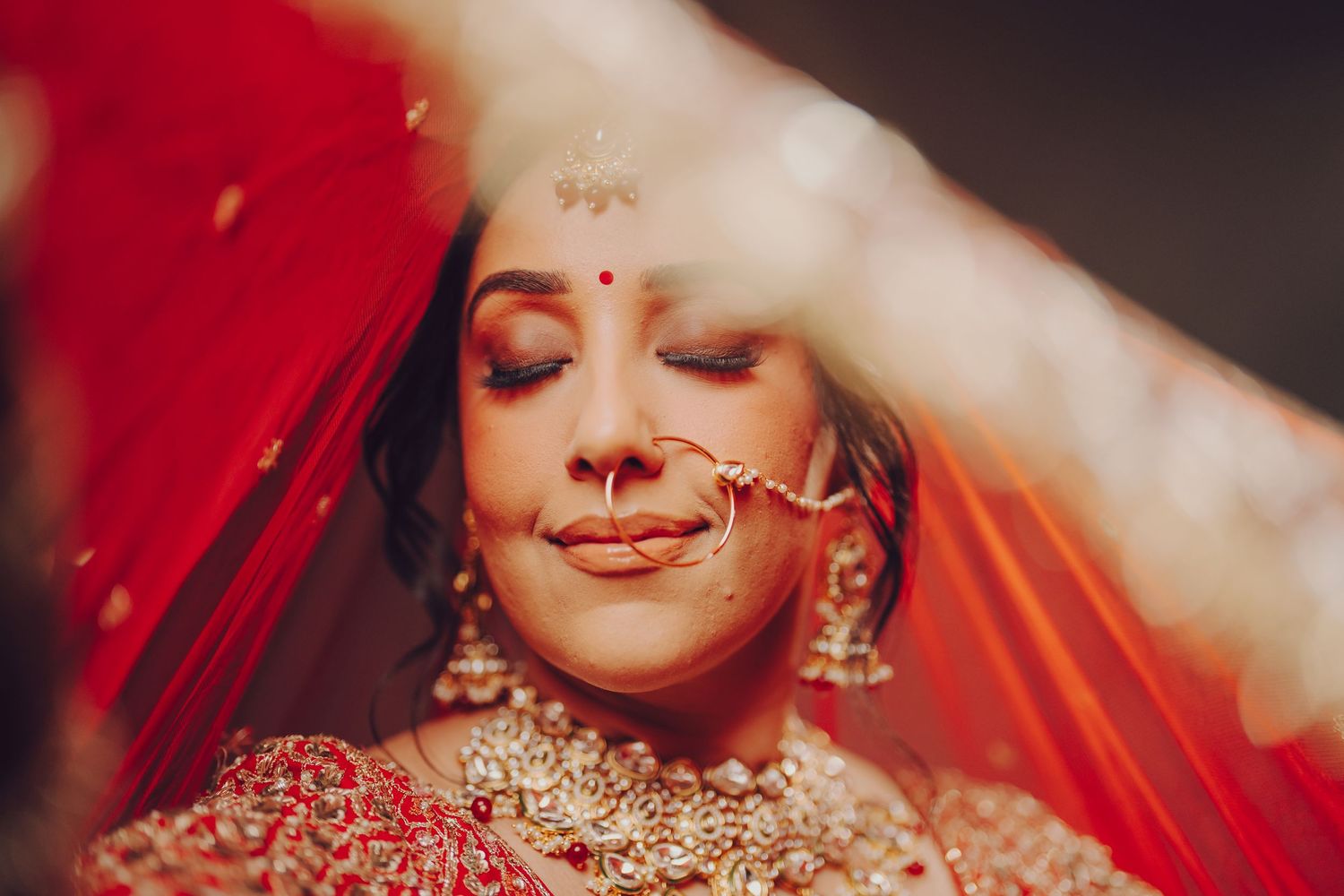 Indian bride in traditional red bridal attire and jewelry smiles during wedding ceremony.