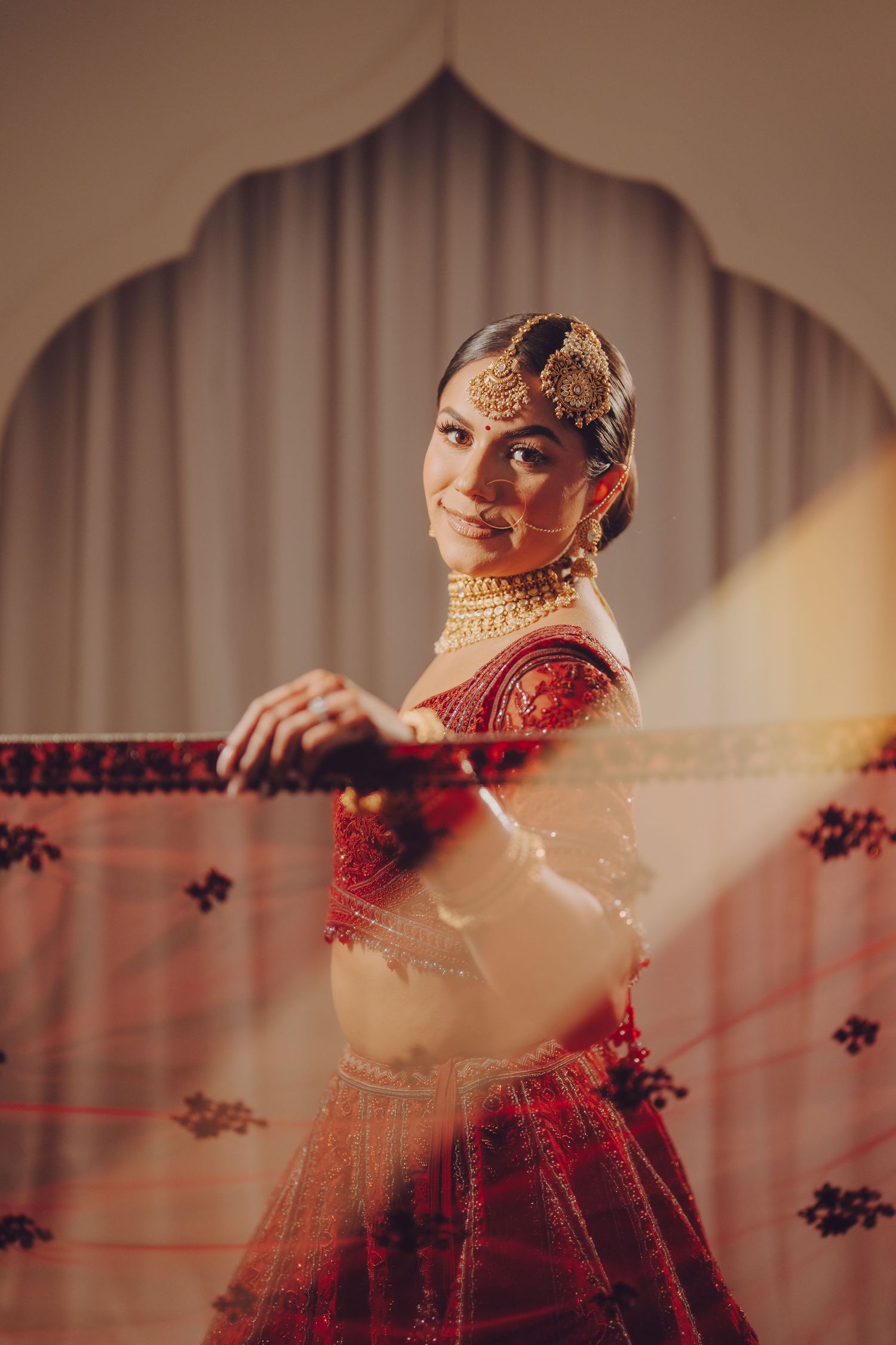 Elegant red bridal lehenga with intricate embroidery and traditional gold jewelry details.
