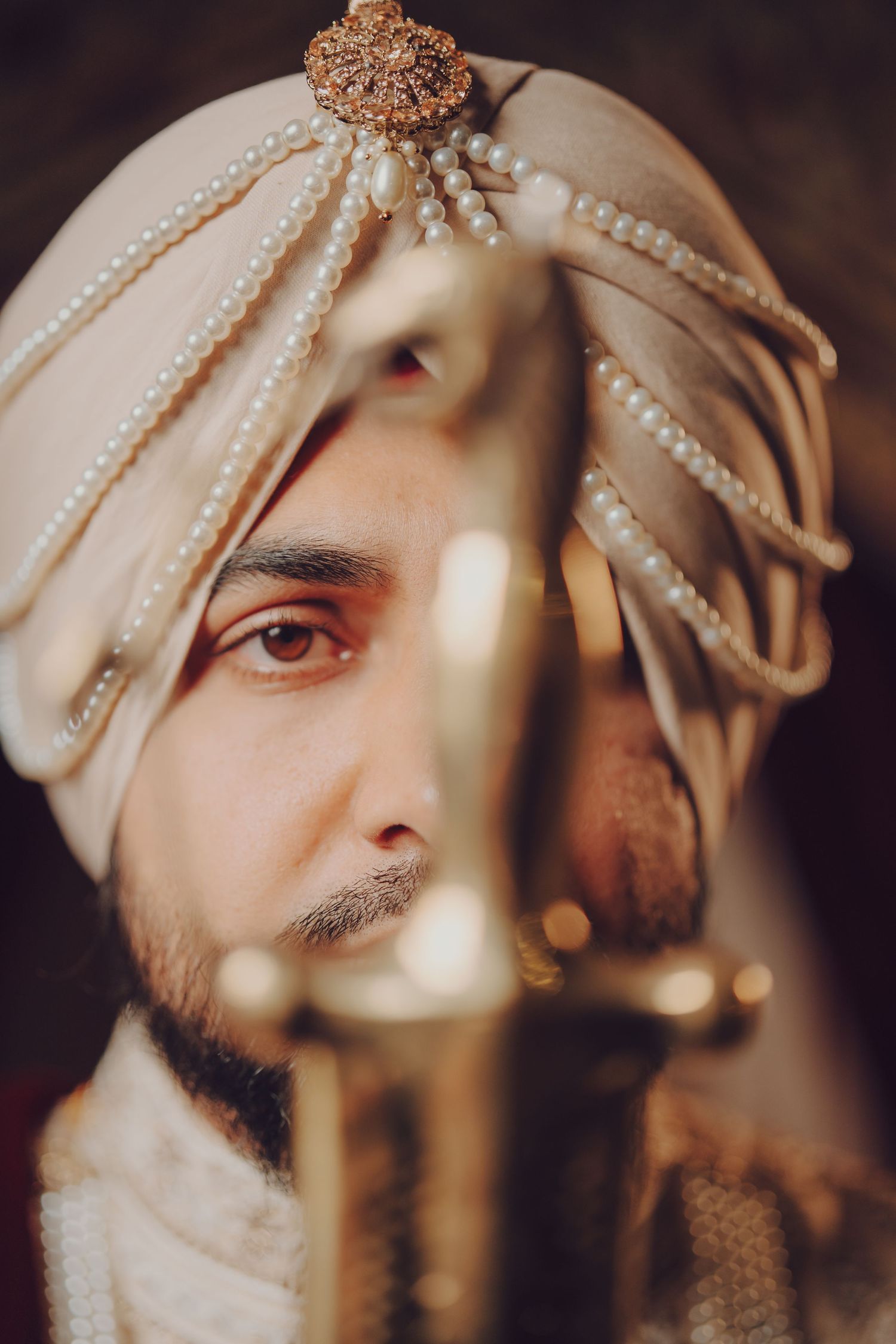 Artistic portrait of traditional Indian groom wearing pearl-adorned turban and formal attire.