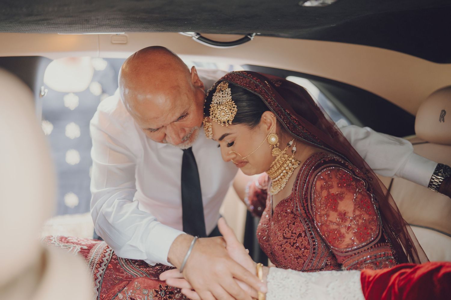 Interior car shot showing traditional Indian wedding attire with burgundy and gold details.