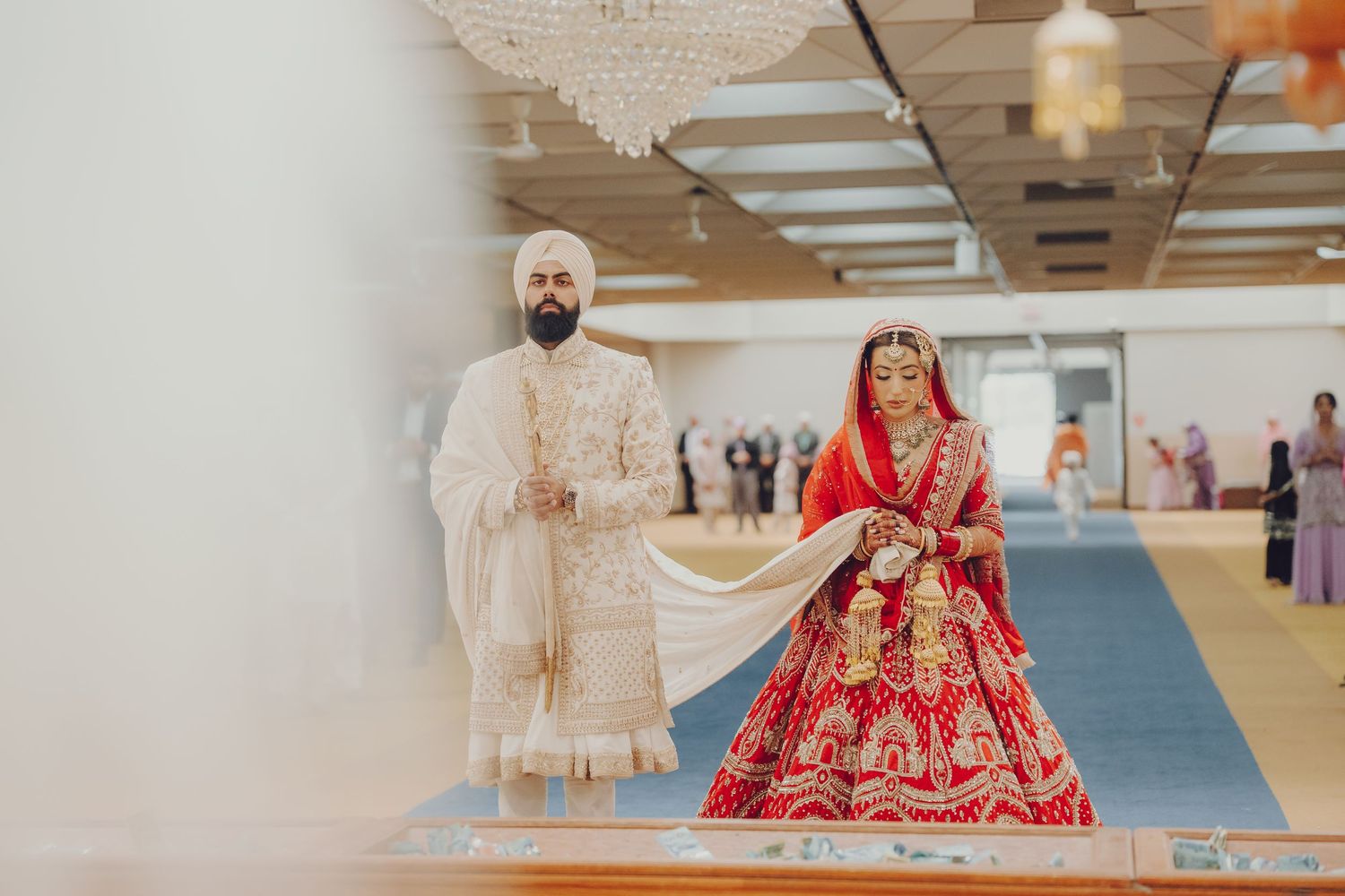 Traditional Sikh wedding ceremony in a modern hall with blue carpet and white decor elements.