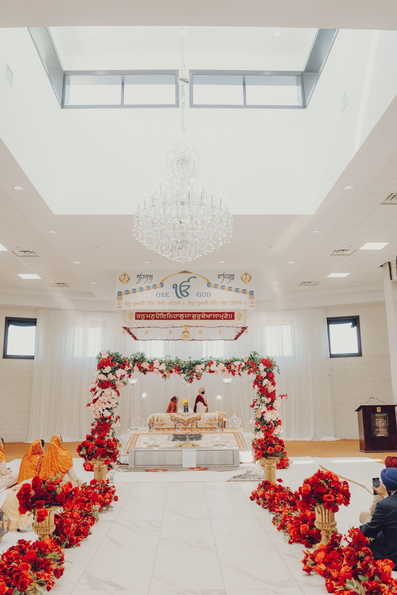 Spacious white wedding venue hall decorated with red floral arrangements and crystal chandeliers.