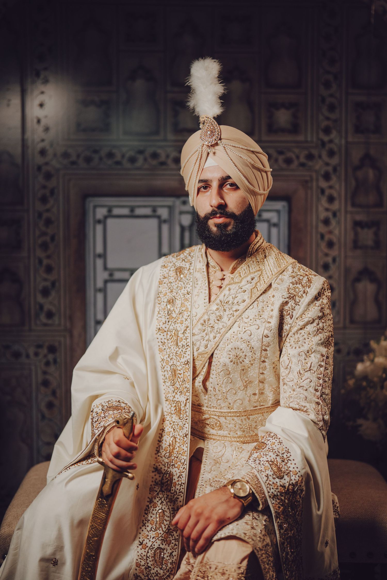 Person wearing cream and gold embroidered traditional wedding attire in an ornate setting.