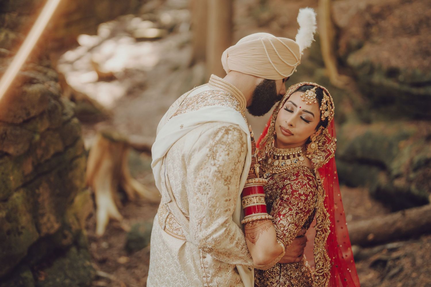 A couple in traditional South Asian wedding attire poses together in a natural outdoor setting.