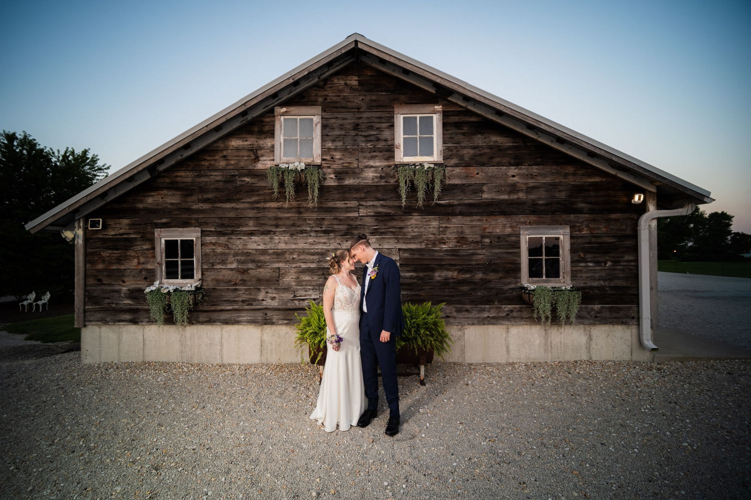 Bride and groom in front of a rustic wooden barn venue at dusk during their wedding celebration. Heritage Prairie Farm Elburn IL