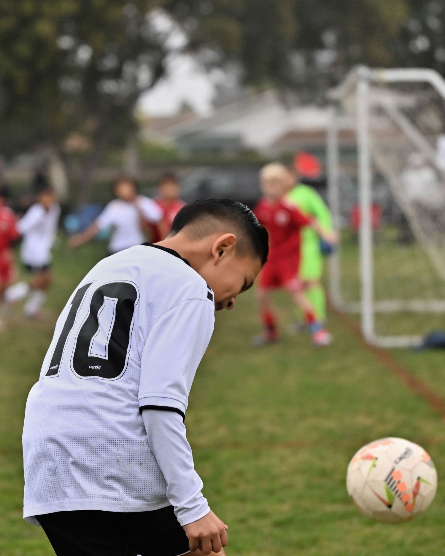 Soccer player in white jersey practices ball control drills on a grassy field during training session.