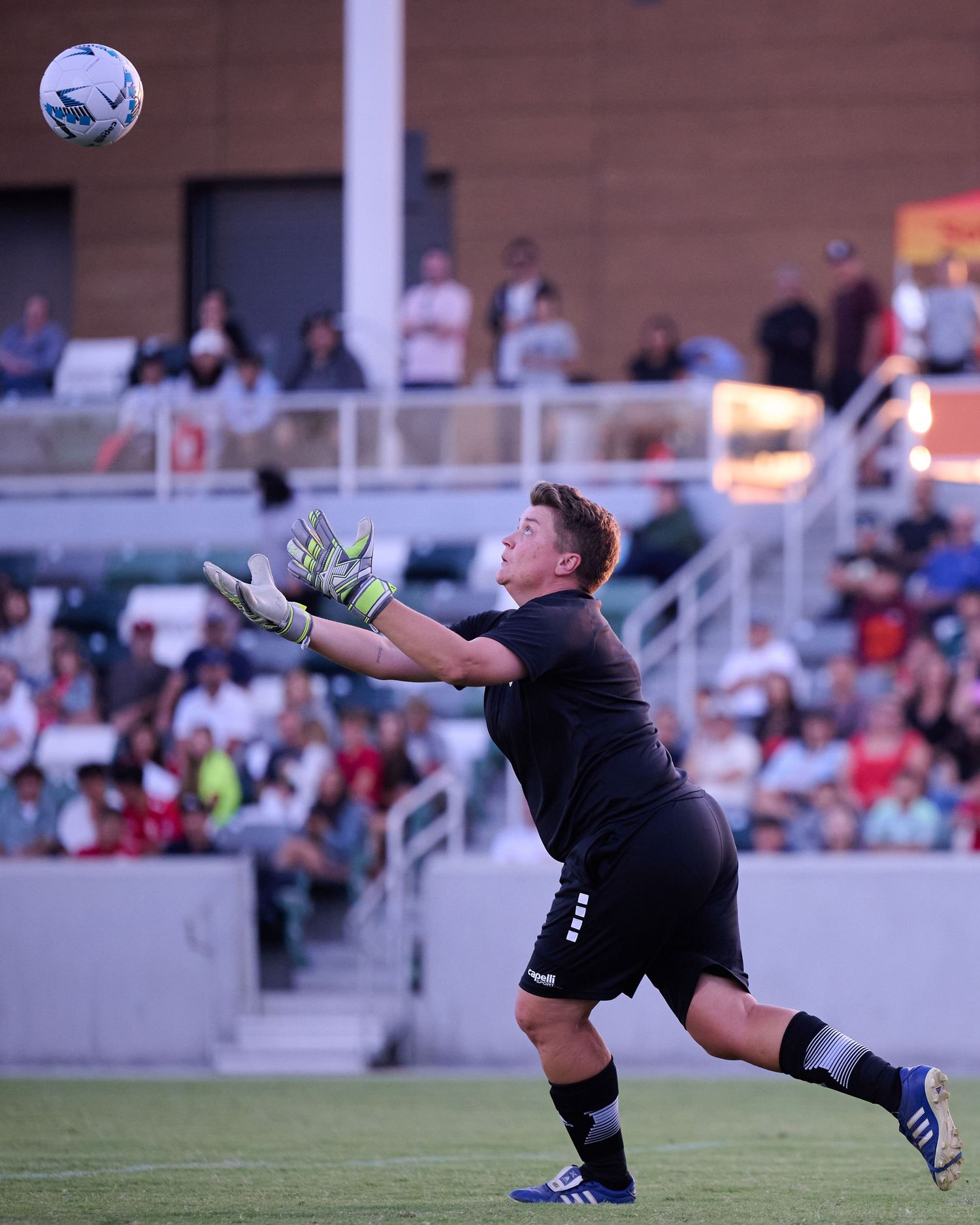 A soccer goalkeeper in black uniform dives sideways to make a dramatic save during a match.
