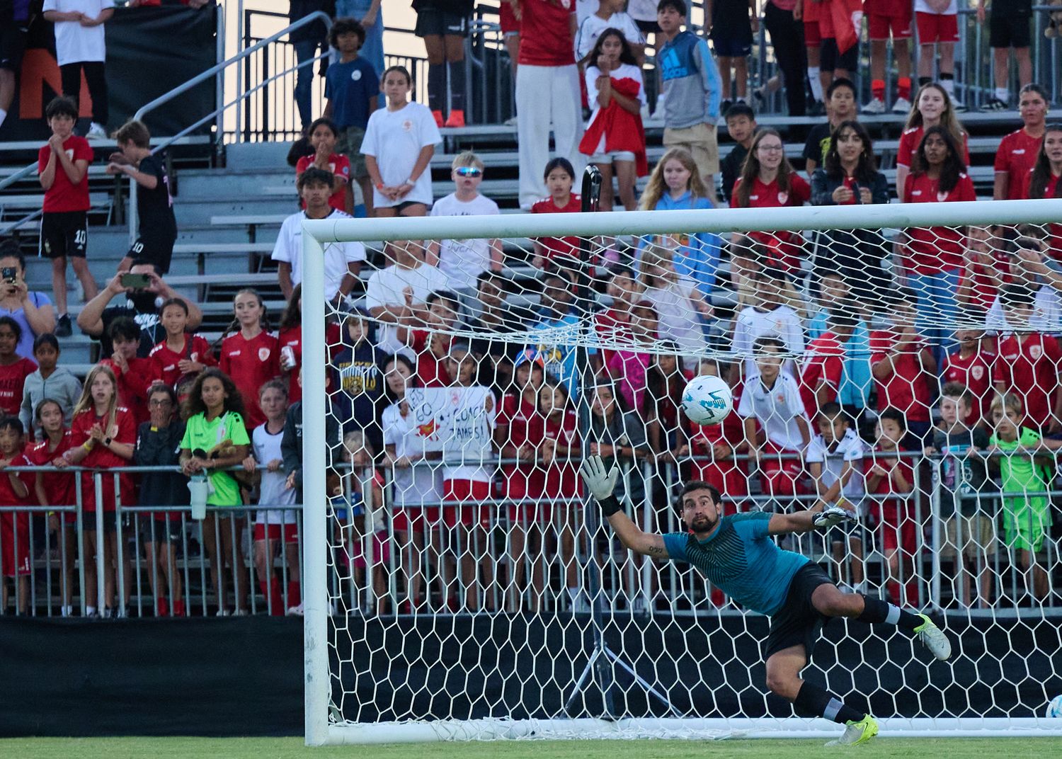 Soccer player jumps high to block a goal attempt during an intense match at a crowded stadium.