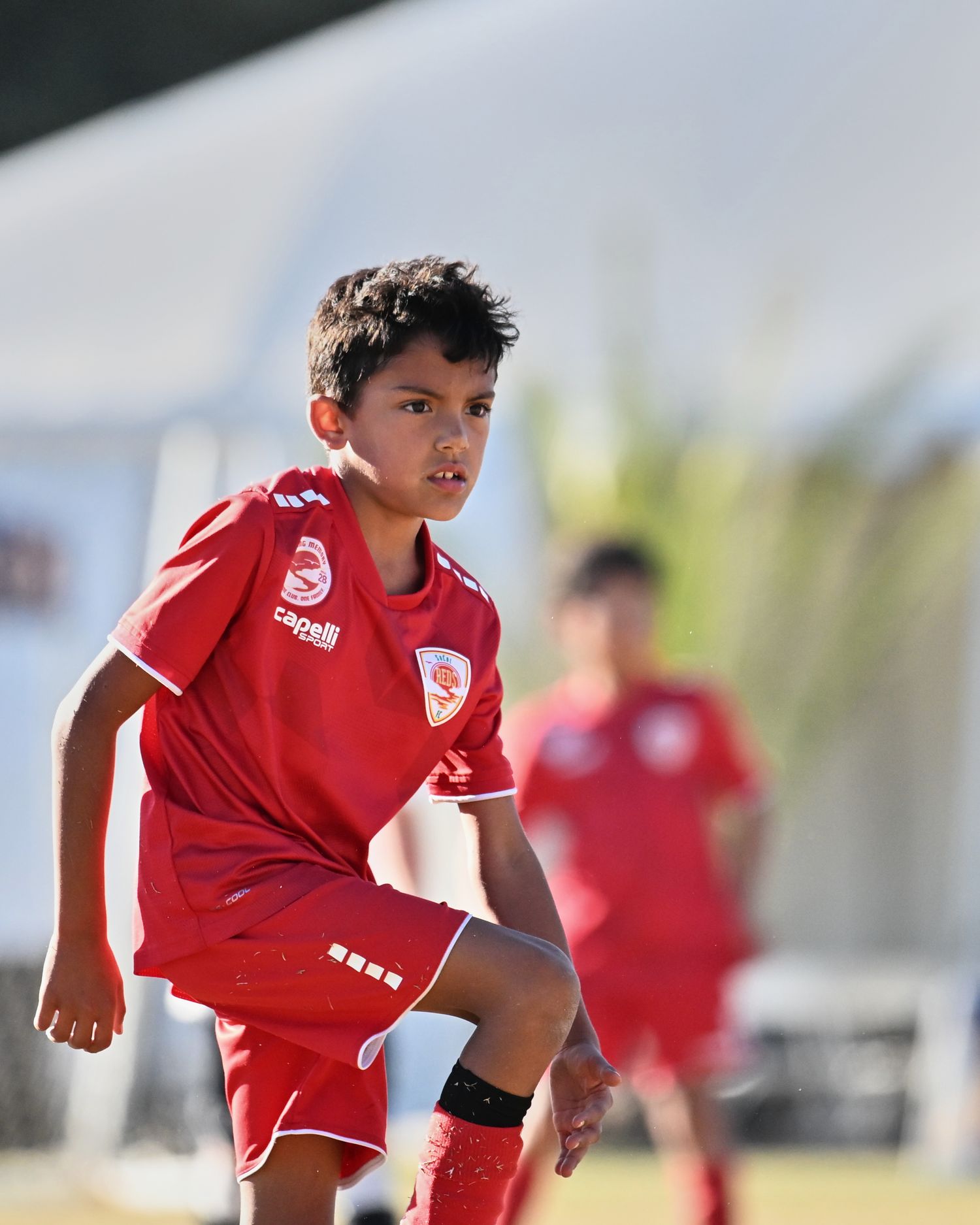 A player in a red uniform practices ball control during soccer training.