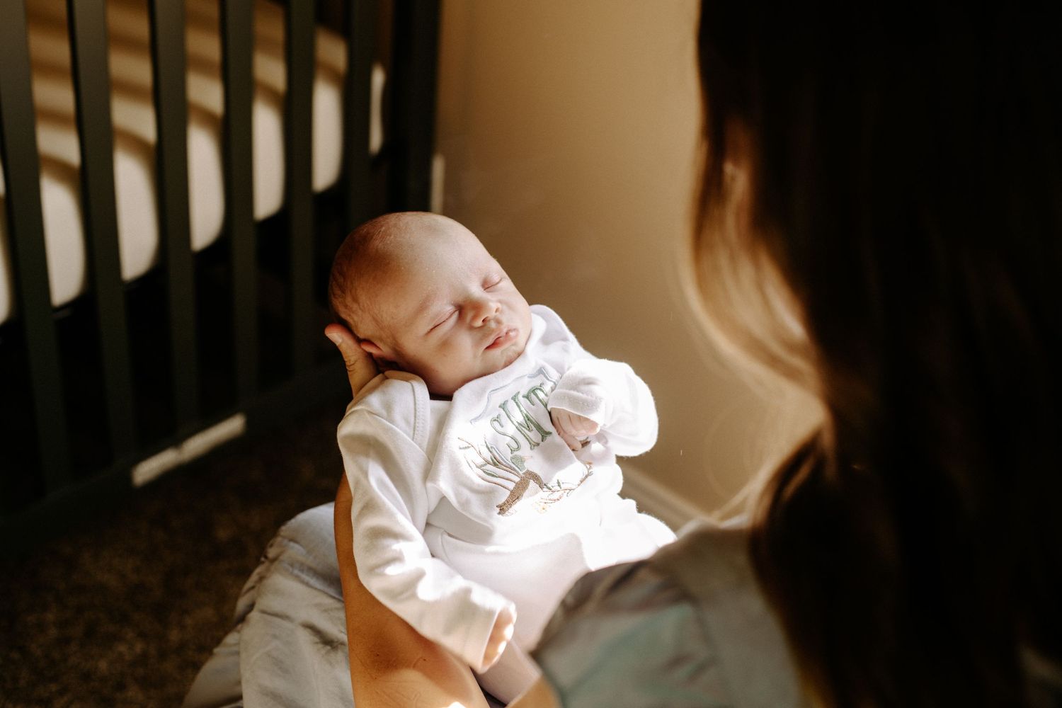 New mom holds her baby, focus is on his face, mom is blurred in the foreground