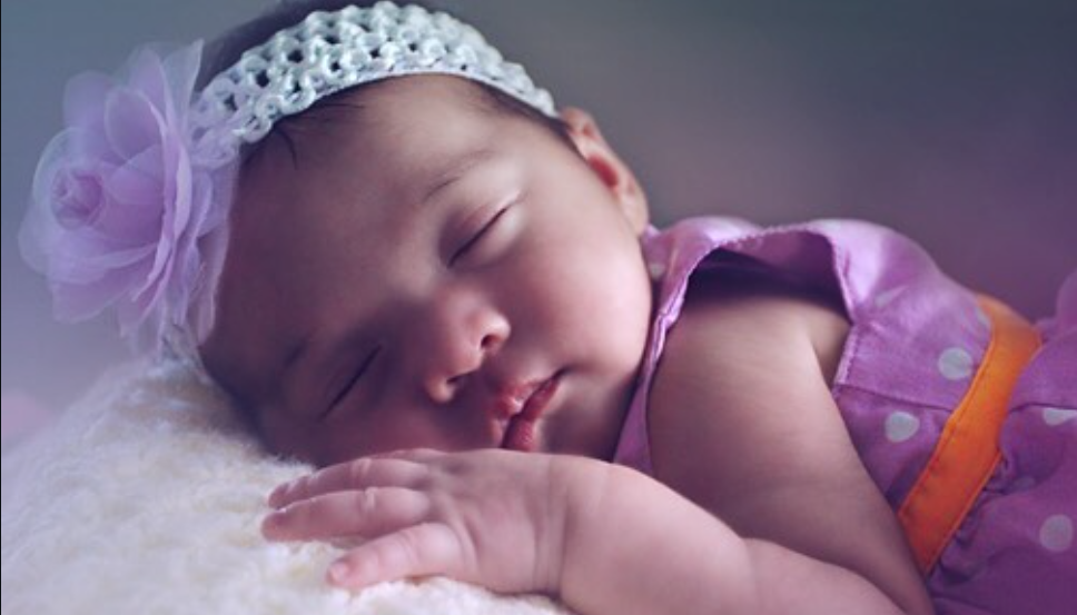 Sleeping baby wearing purple tulle dress in dreamy studio lighting.