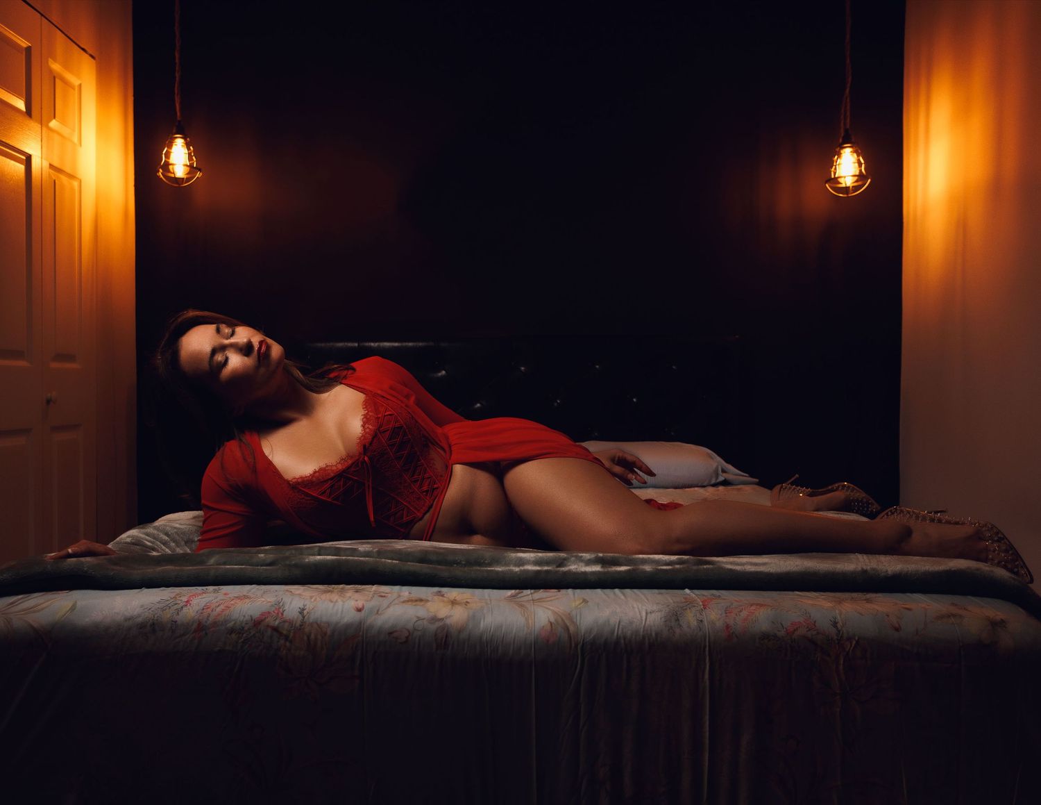 Sensual portrait on bed with warm lighting from wall sconces.
