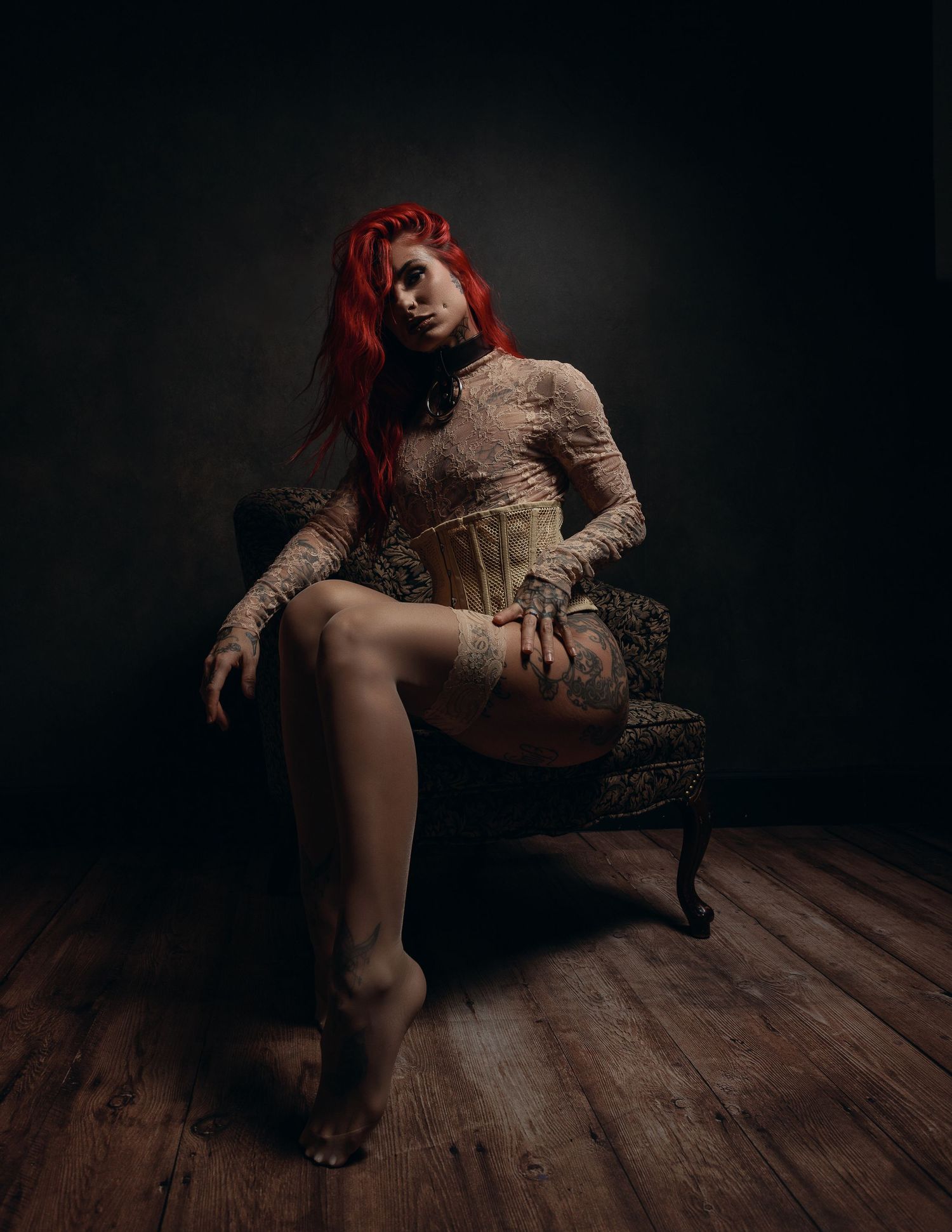 Moody boudoir photography with red-tinted lighting on hardwood floor.