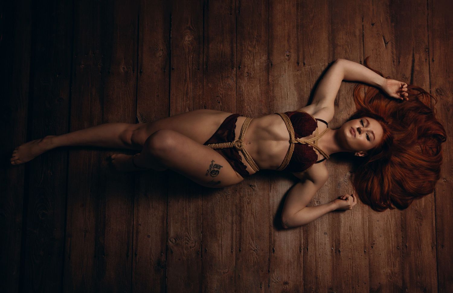 Moody boudoir portrait with black lingerie on wooden floor.