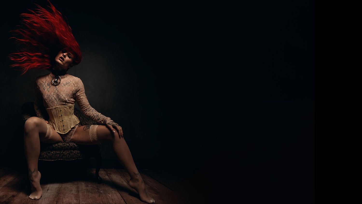 Artistic boudoir photo with red feather headpiece in dark moody lighting.