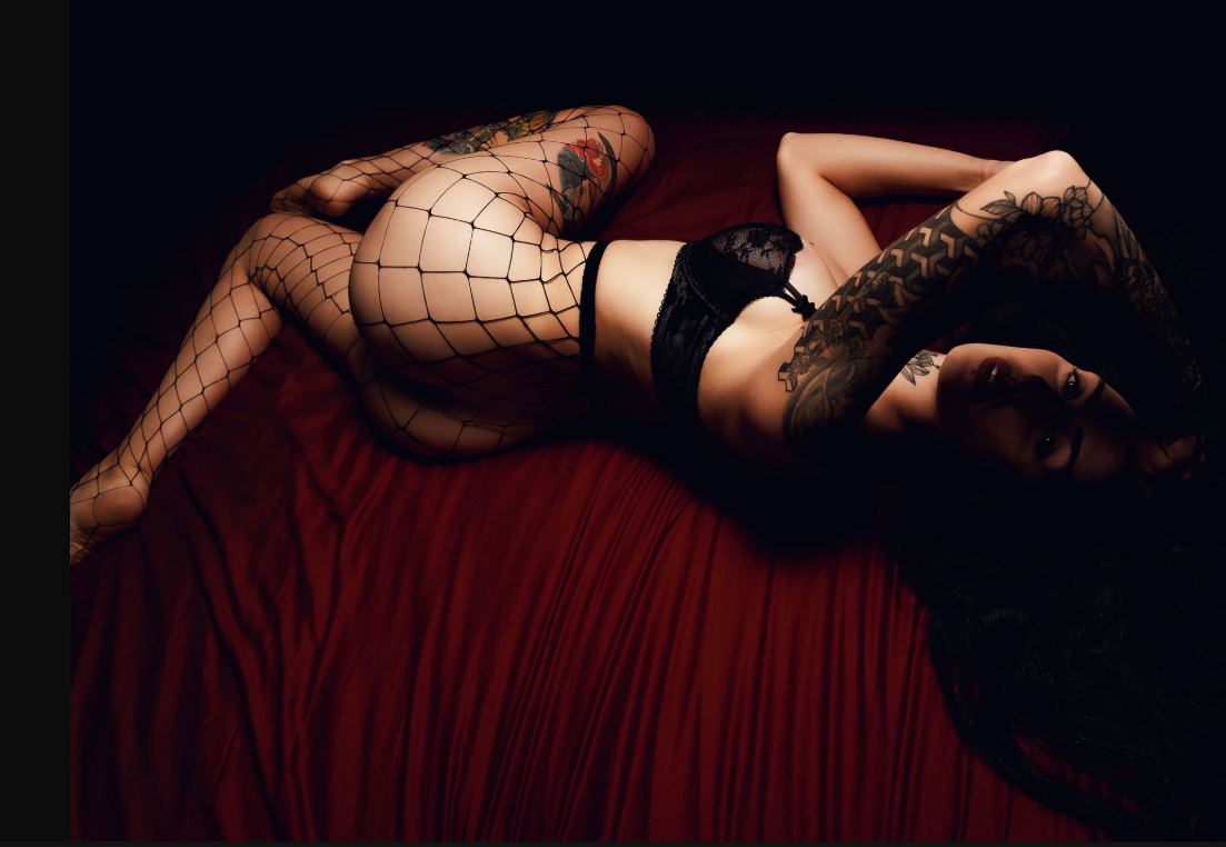 Artistic boudoir photoshoot with dark moody lighting on red velvet furniture.