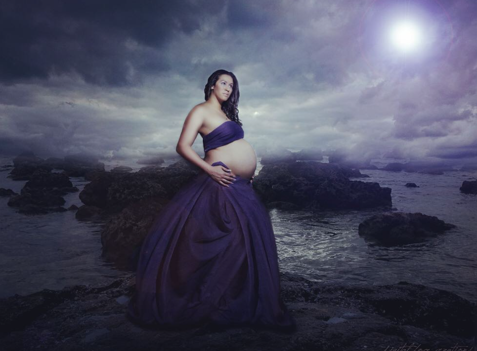 Dramatic maternity portrait in purple gown against stormy coastal landscape.
