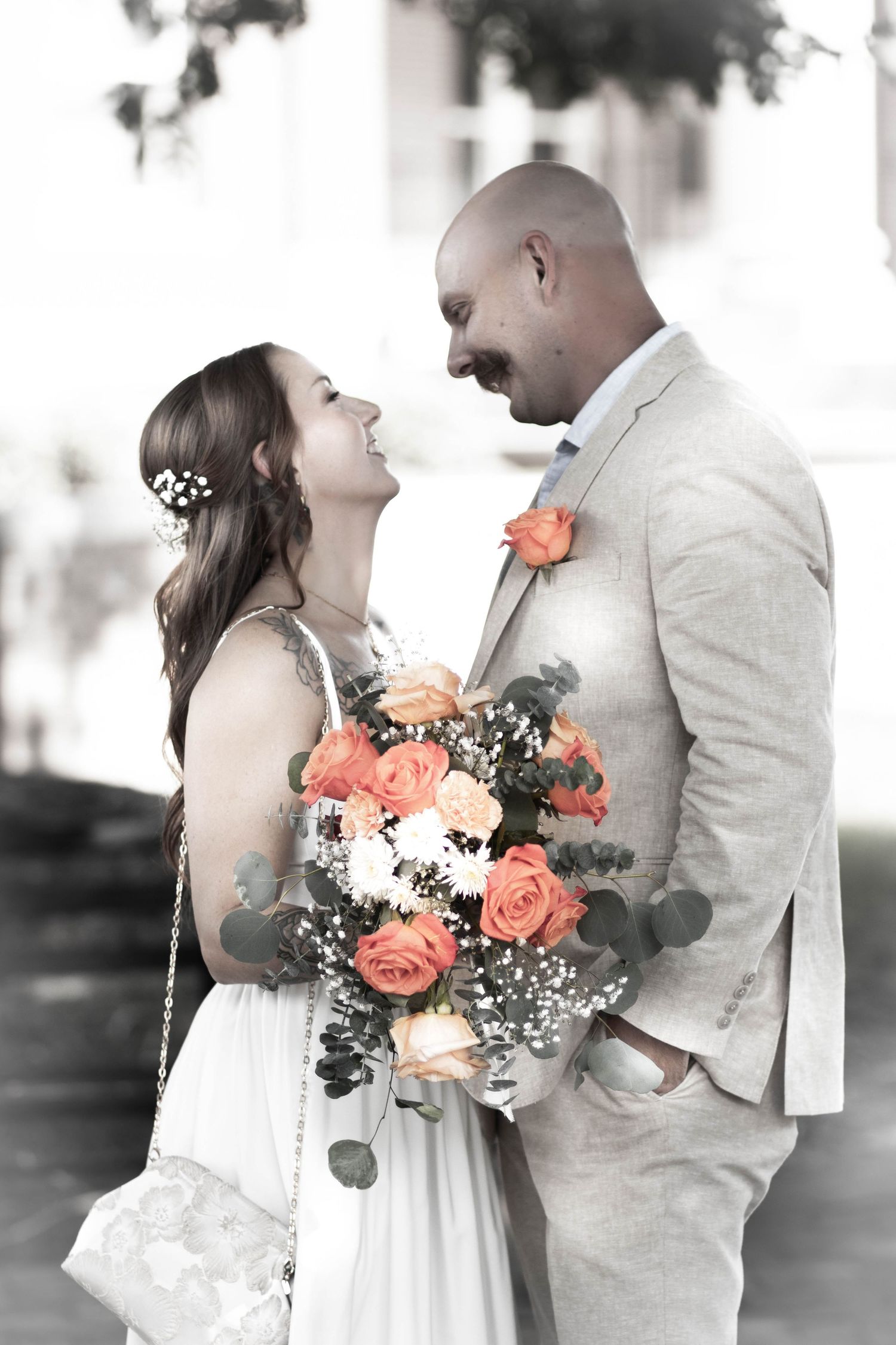 Black and white photo of bride and groom sharing romantic moment with colorful orange rose bouquet highlighted.
