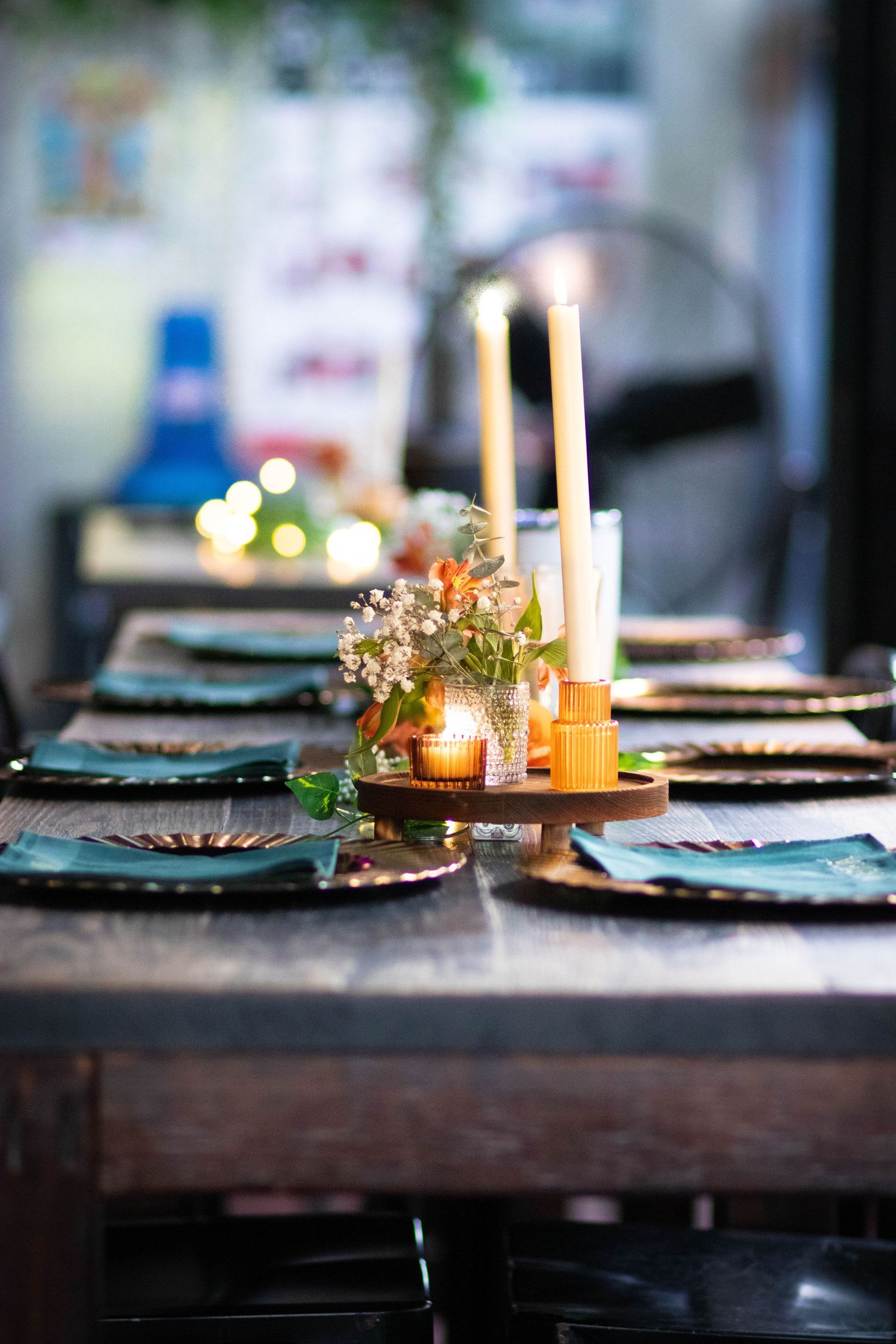 Elegant rustic dining table set with candles, greenery centerpiece, teal napkins, and gold chargers for an intimate dinner.