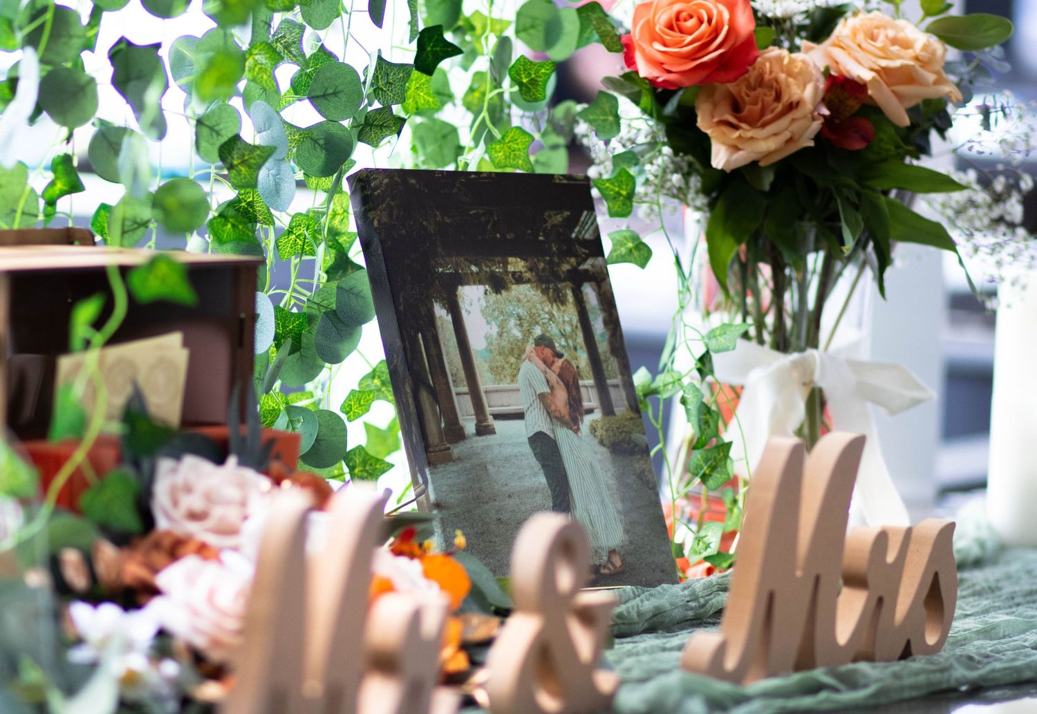 Wedding reception table decor with framed couple photo, Mr and Mrs wooden signs, roses bouquet, and green ivy garland.