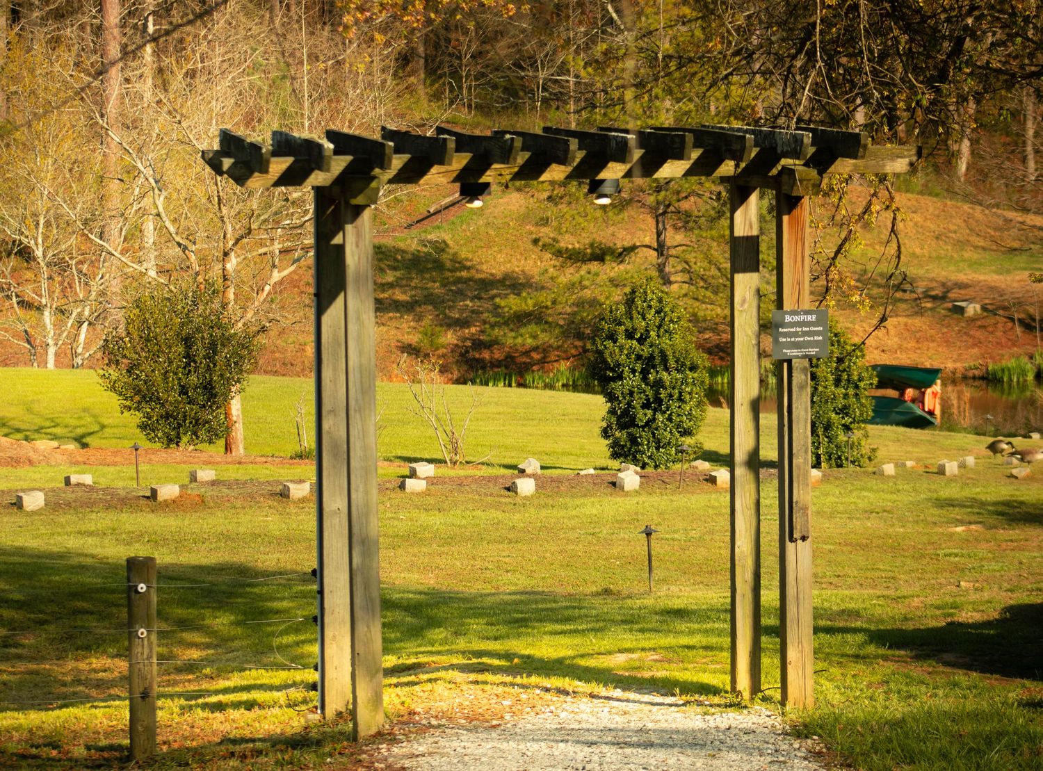 Wooden pergola gate entrance leading to a scenic green park with stone markers and evergreen trees in autumn.
