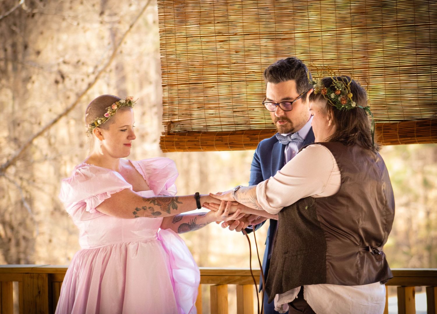 Bride in pink gown and groom exchange vows with officiant during intimate outdoor wedding ceremony.
