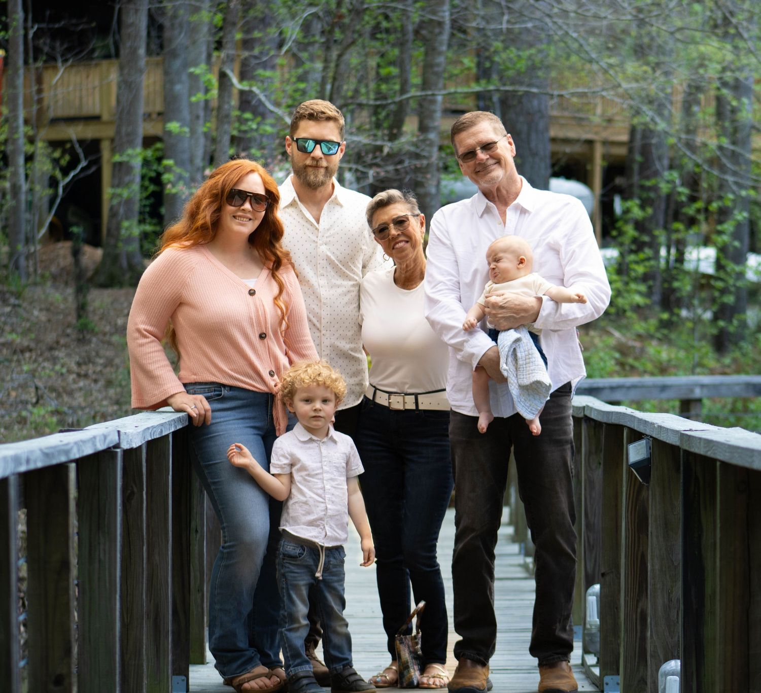 Happy multi-generational family with redhead woman, tall man, older couple, and two children on bridge.