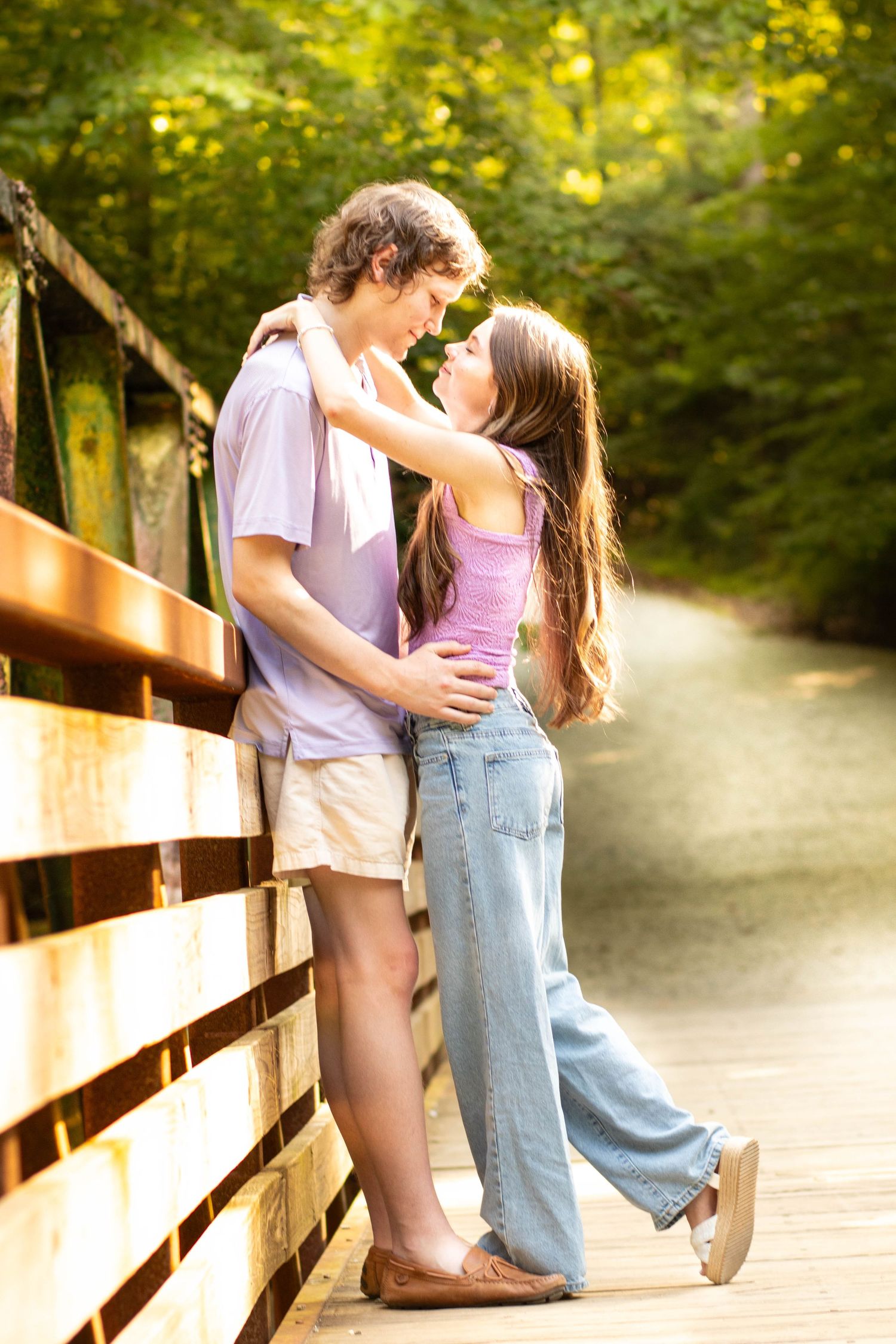 Young couple sharing a romantic moment on a wooden bridge surrounded by lush green trees in summer.