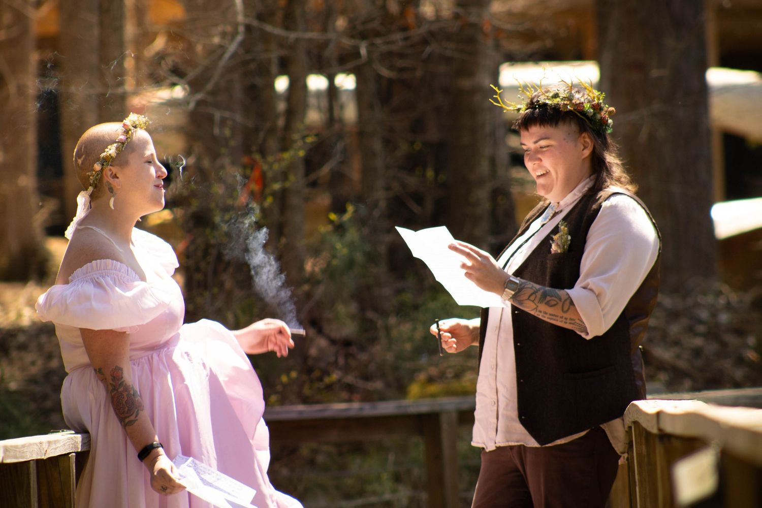 Outdoor wedding ceremony with bride in pink dress and officiant reading vows, surrounded by autumn trees.