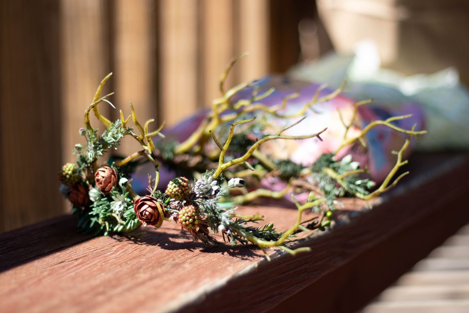 Decorative floral crowns with pine cones and greenery rest on a wooden surface.