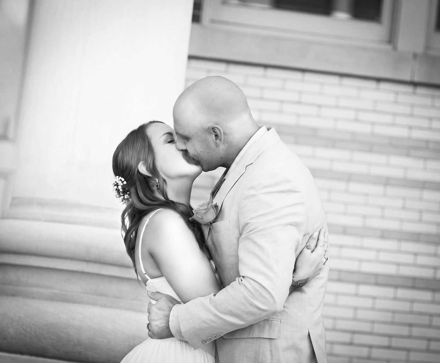 Black and white photo of a couple sharing a romantic kiss at their wedding ceremony outdoors.