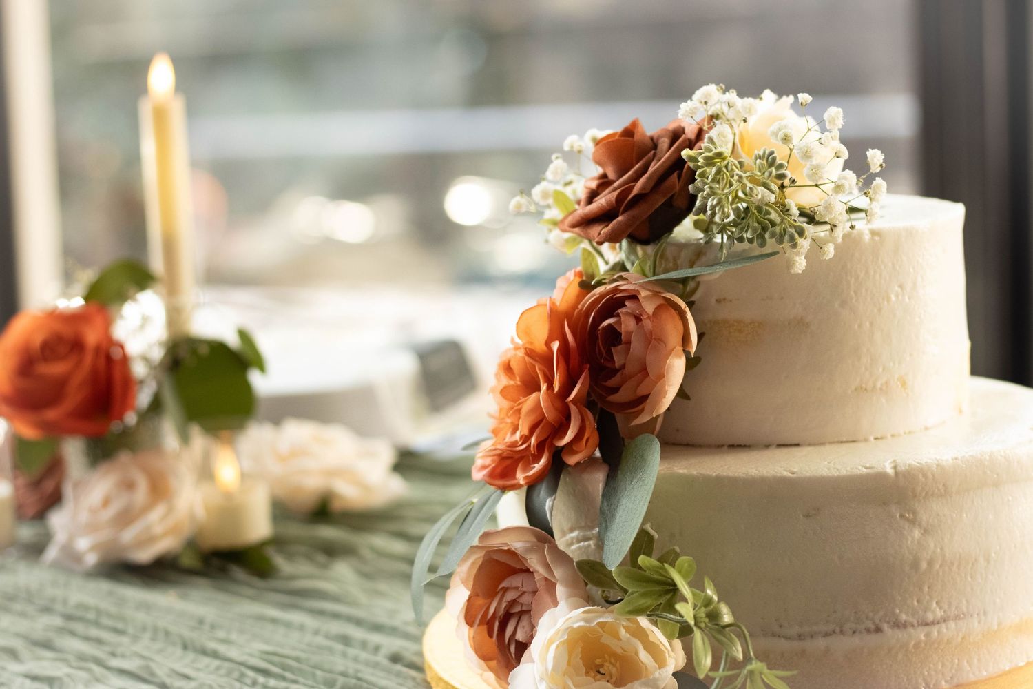 Elegant white two-tier wedding cake adorned with orange and cream roses, with a candle in the background.
