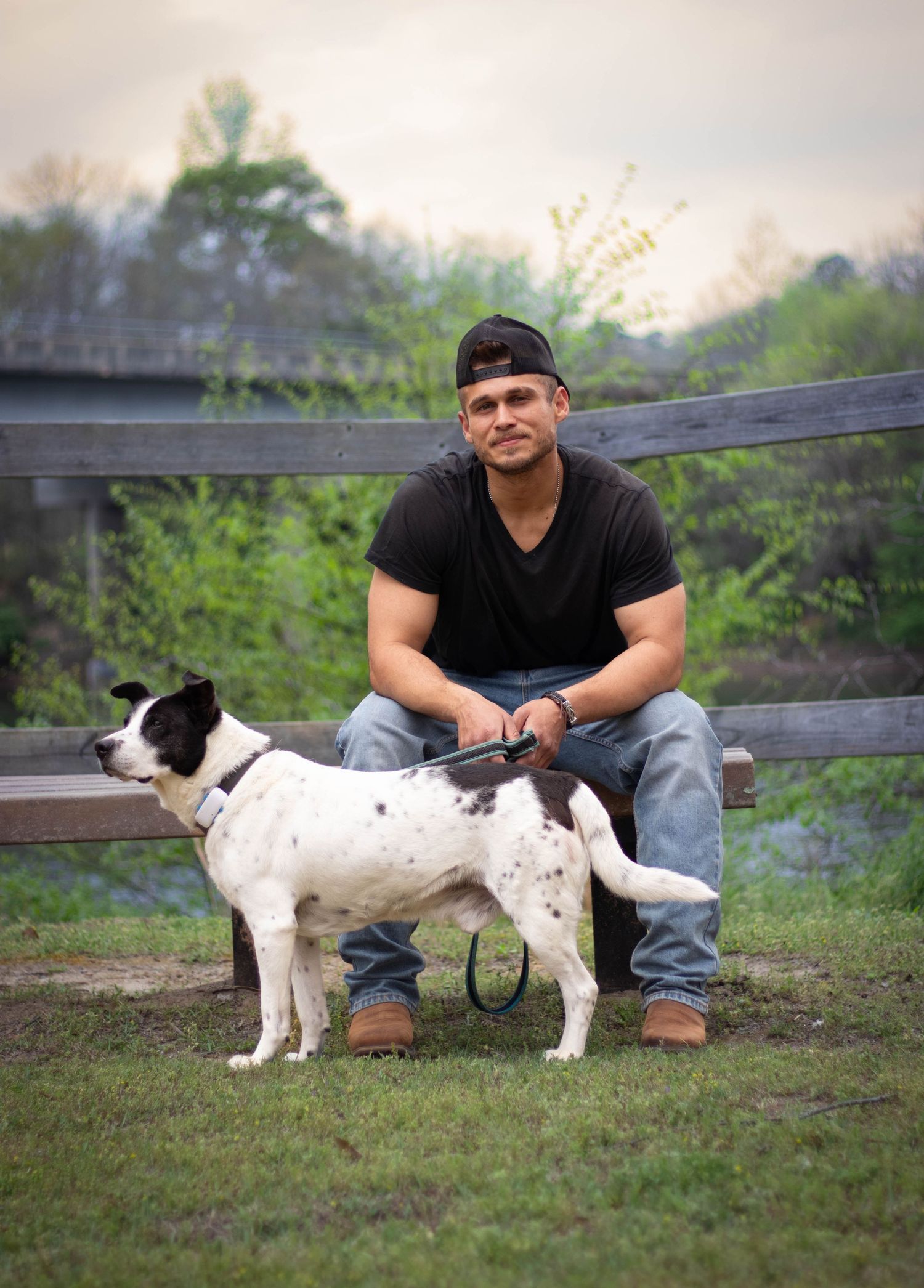 Young man sitting on a fence with his black and white spotted dog in a rural setting.