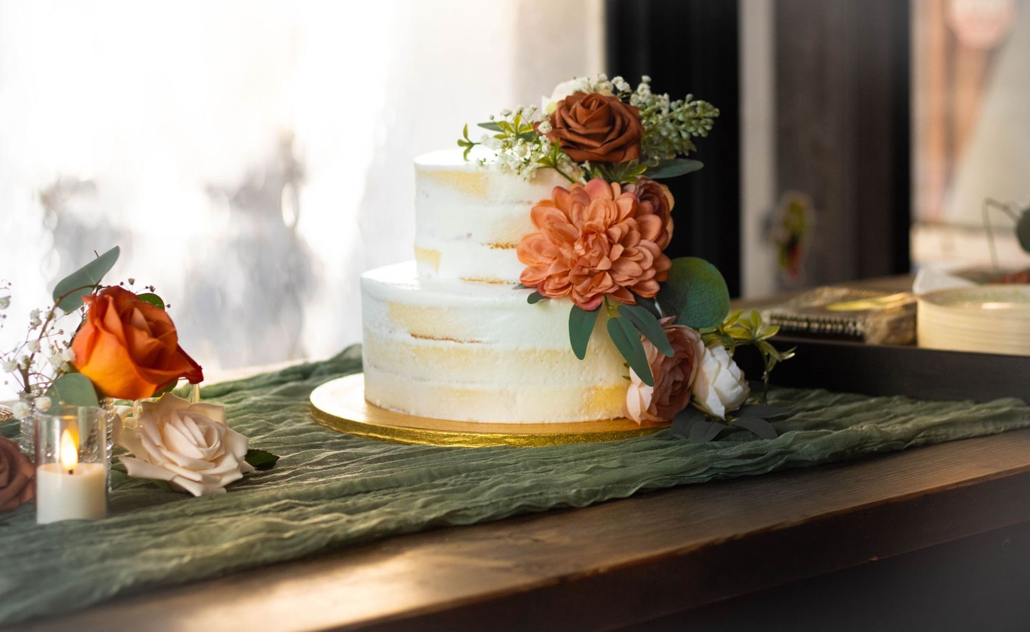 Elegant two-tier white wedding cake with peach dahlias and roses on a rustic wooden table.