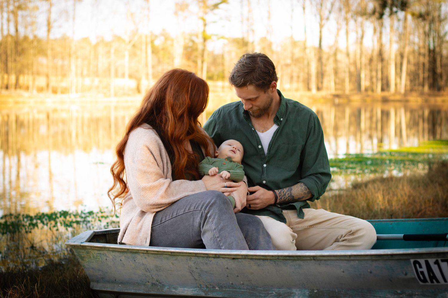 Couple sitting in boat on lake holding newborn baby together.