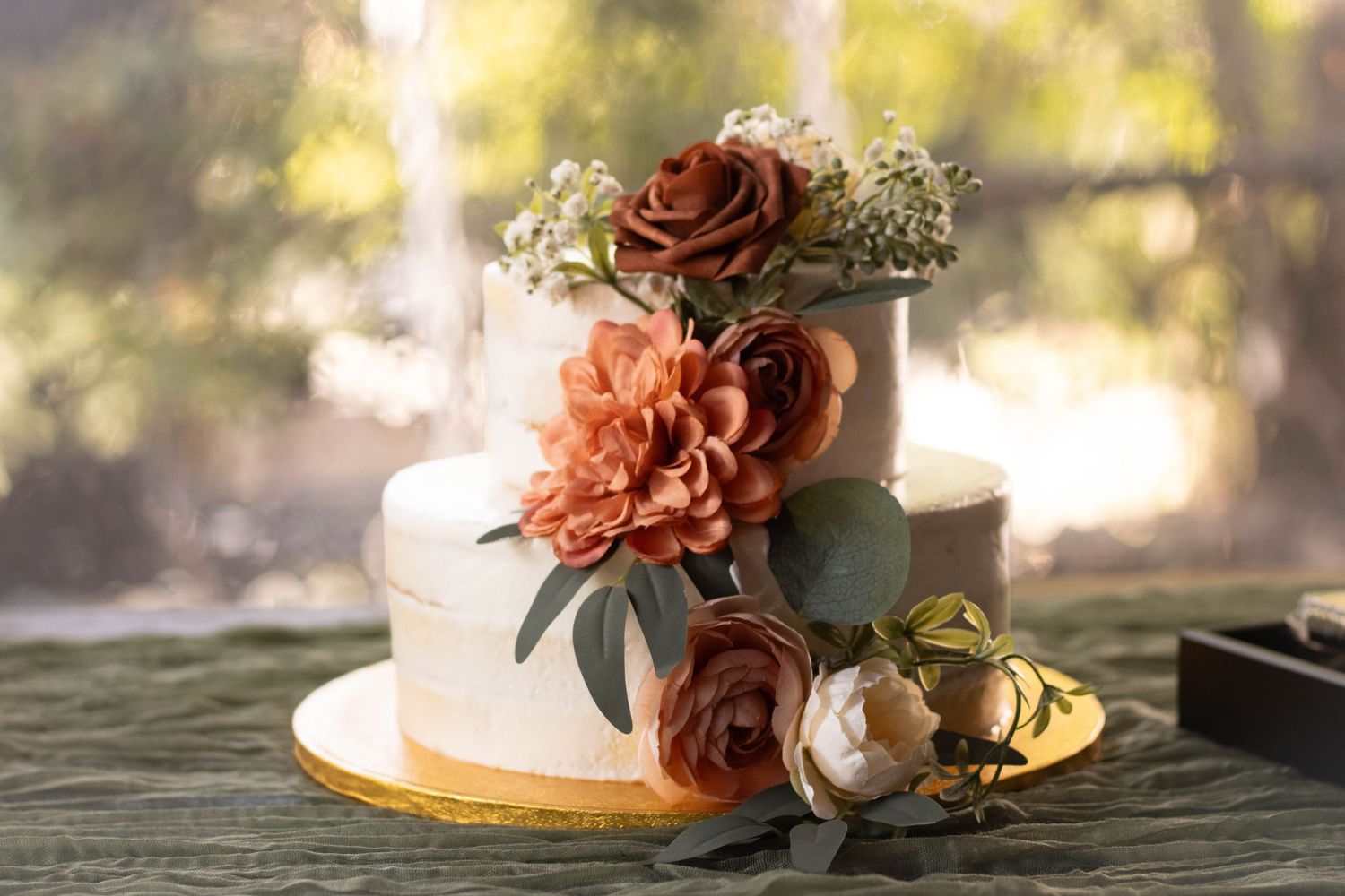 Elegant two-tier white wedding cake adorned with rust roses, dahlias, and greenery.