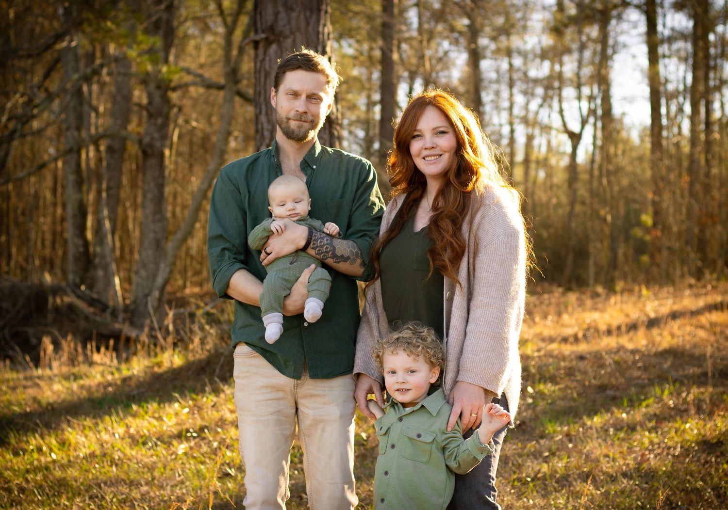 Happy family of four posing in a sunny autumn forest with golden leaves.