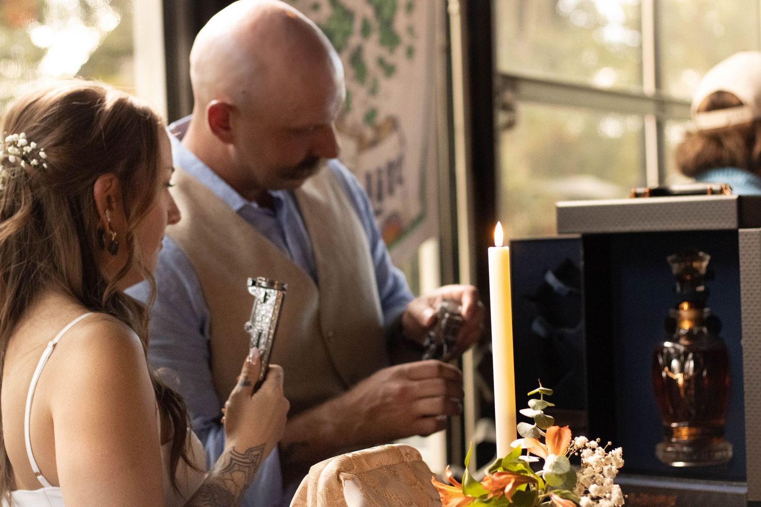 Bride and groom examining a decorative whiskey bottle display at their wedding reception.